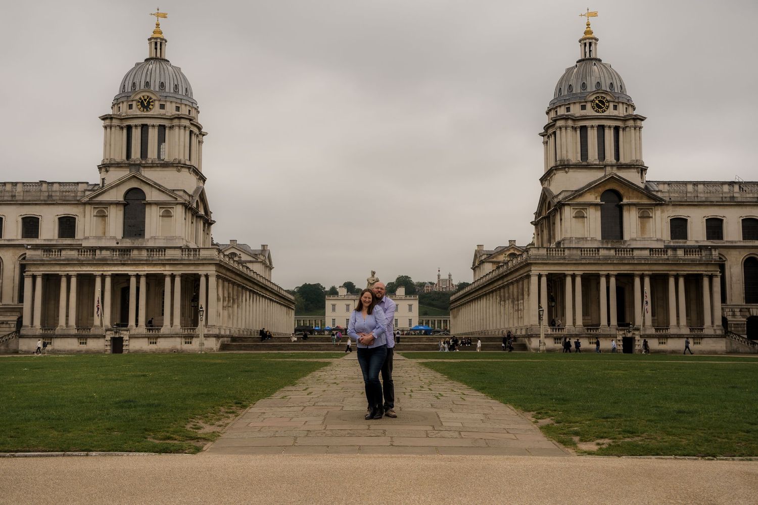 A couple poses in front of the symmetrical domed towers of the Greenwich Naval College.