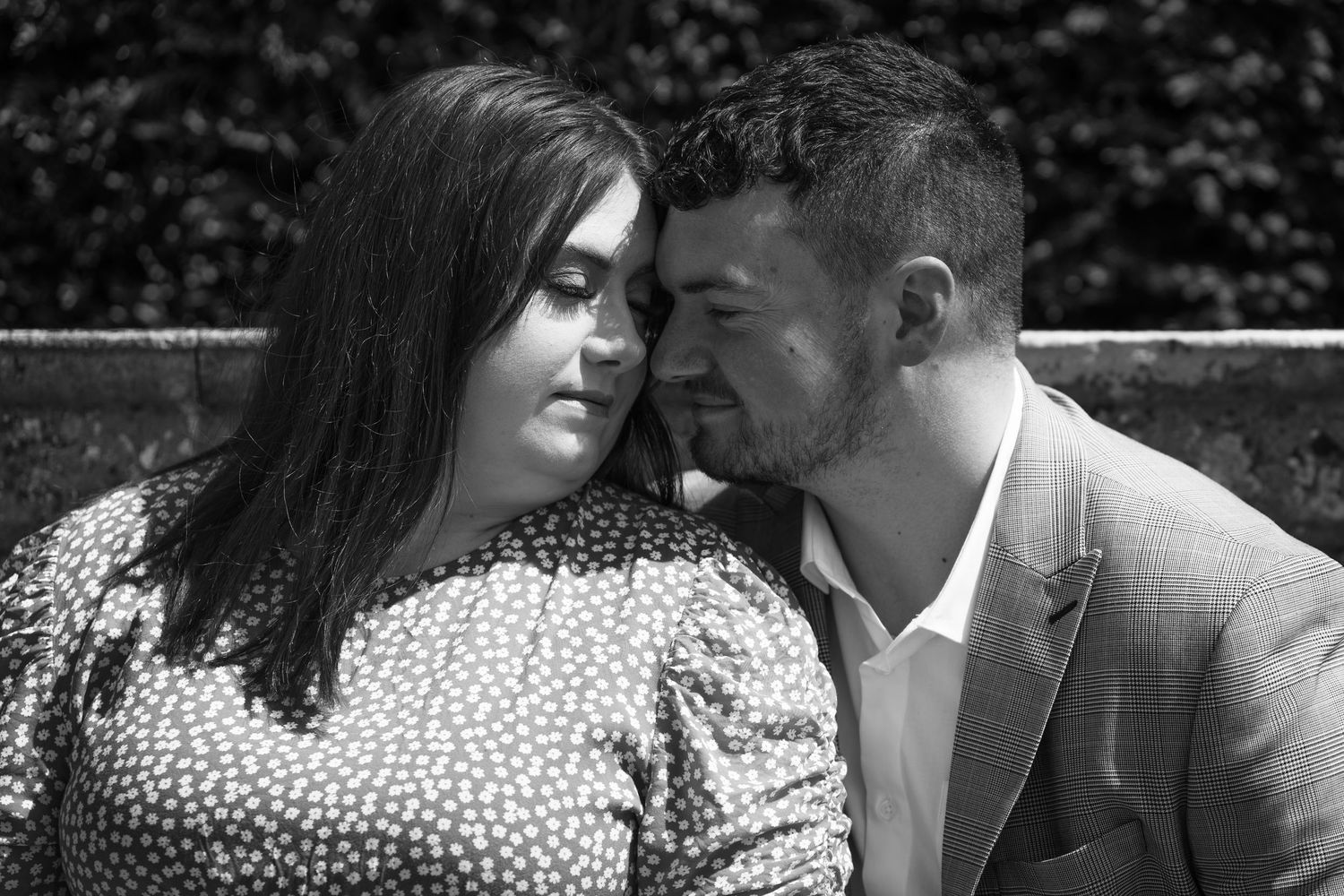 An intimate black and white portrait of a couple sharing a tender moment outdoors.