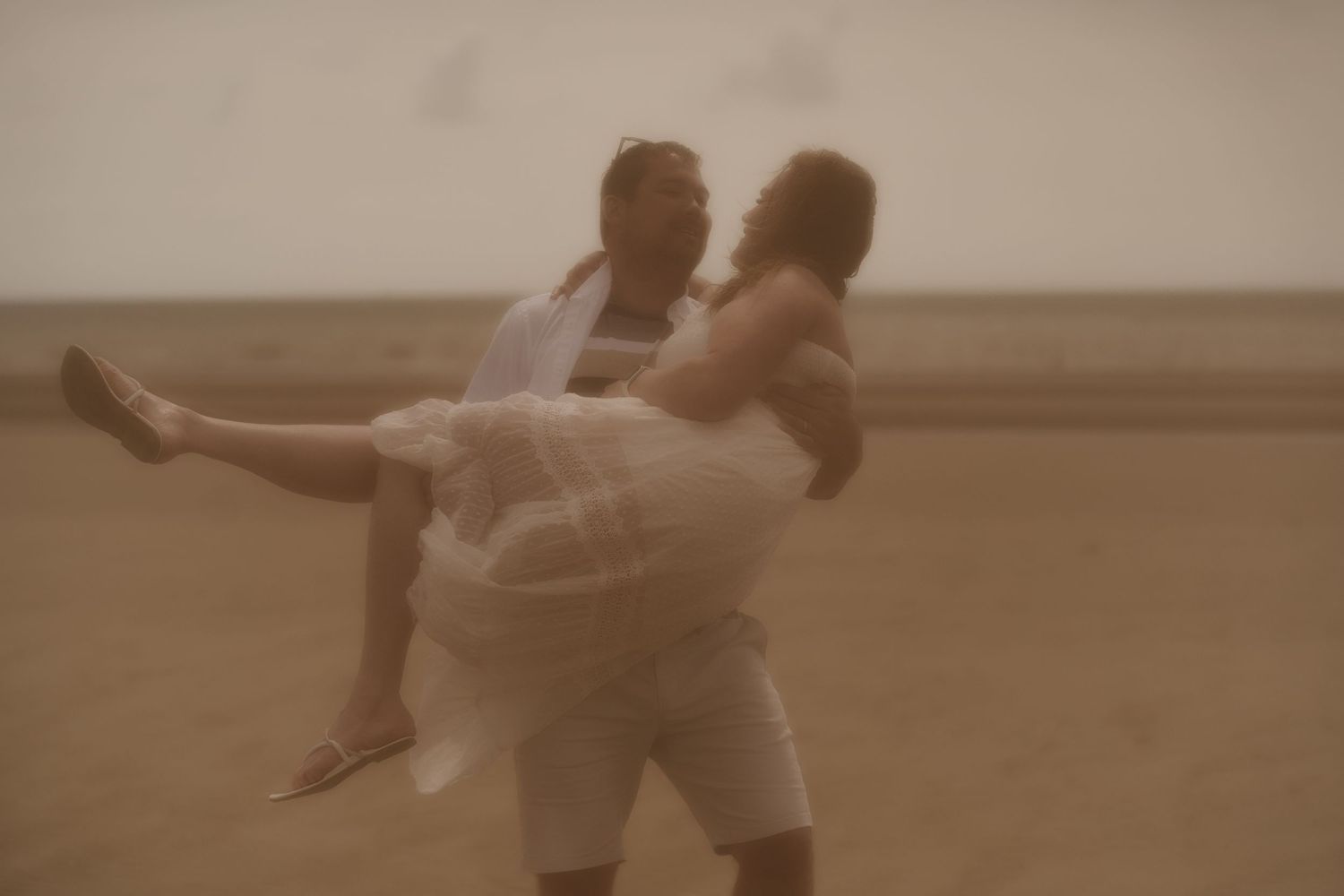 A dreamy sepia-toned photo of a couple embracing on a beach with a romantic, soft-focus effect.