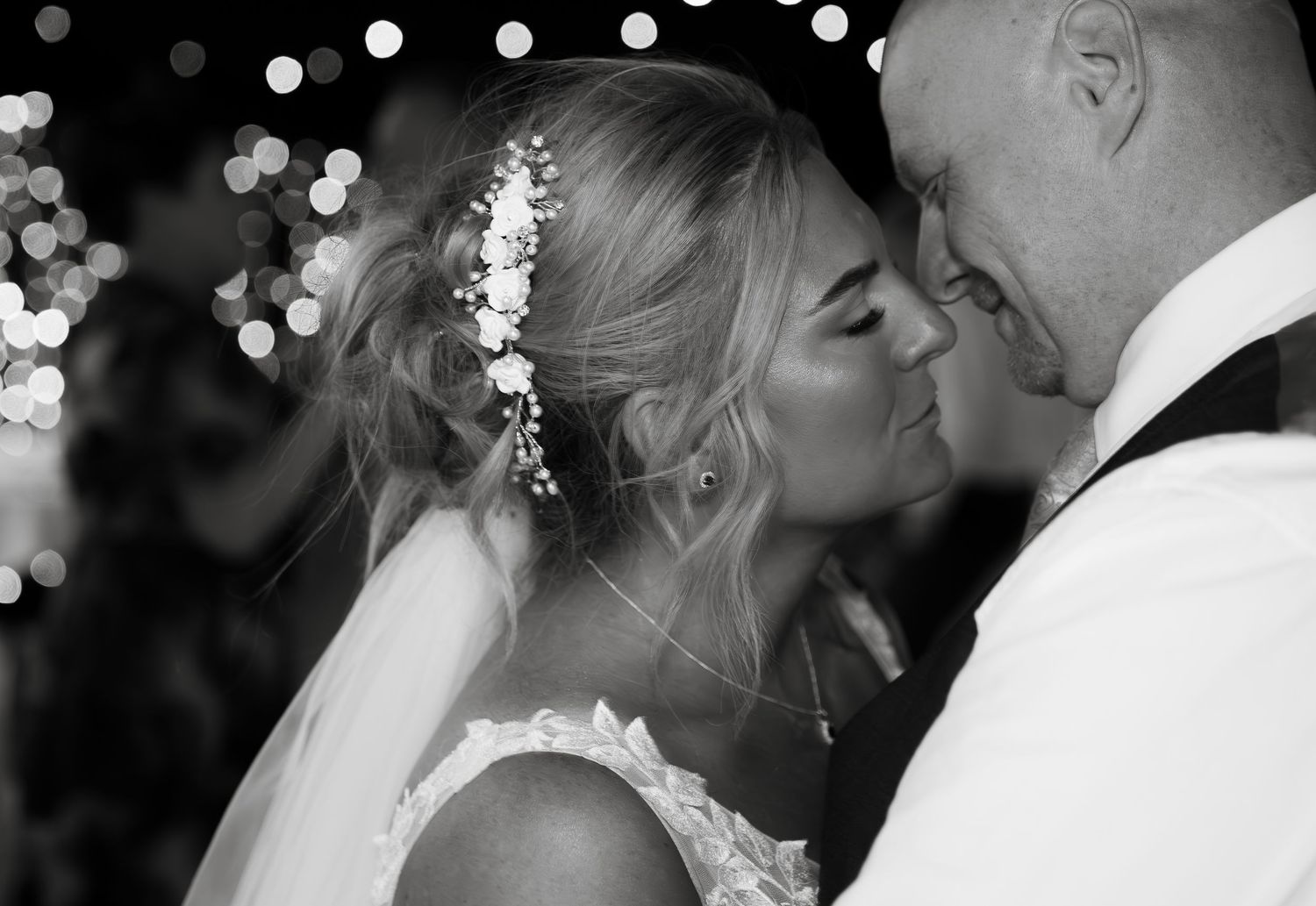 Black and white image of newlyweds sharing an intimate moment in front of bokeh lights.