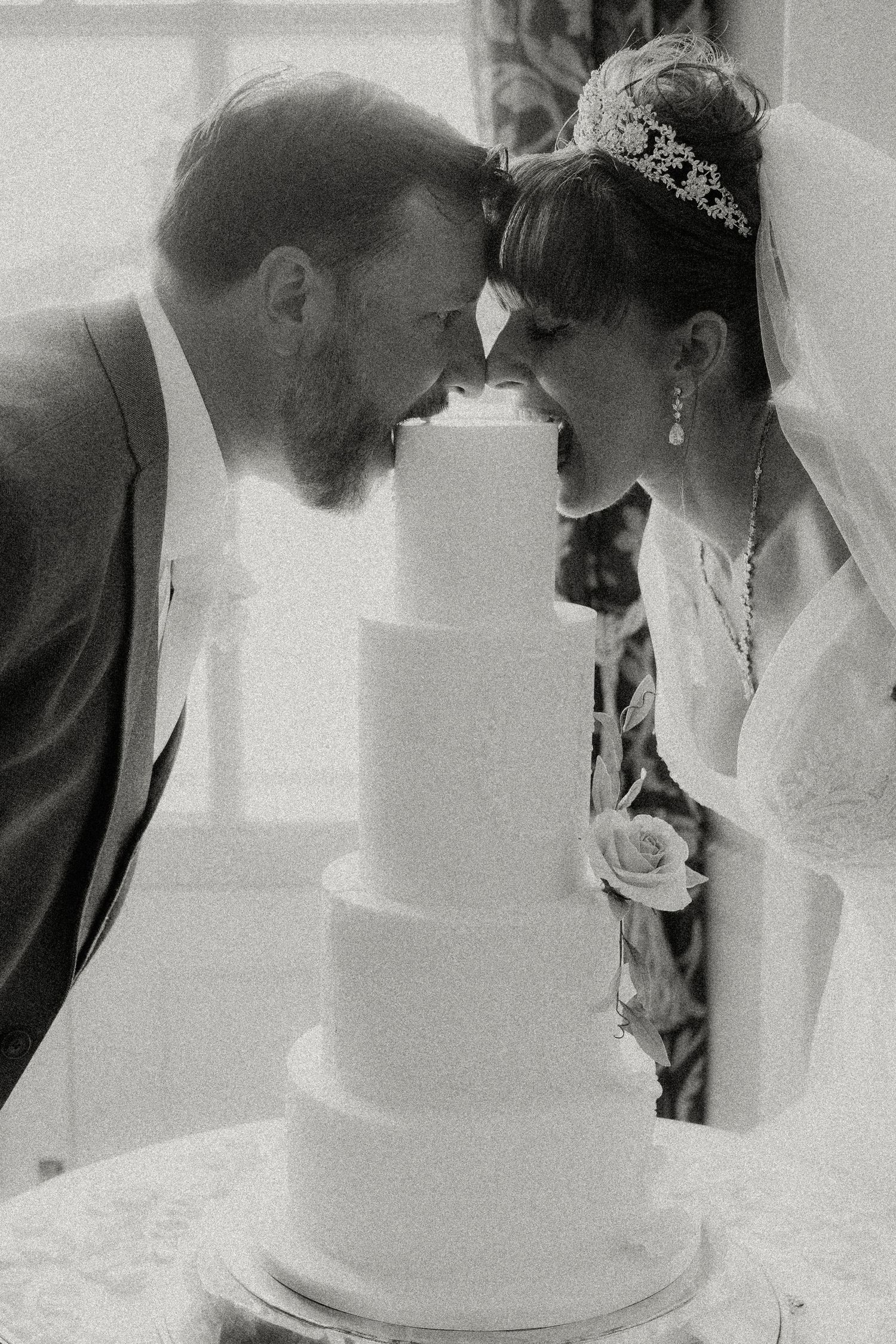 A romantic black and white photo of newlyweds sharing an intimate moment by their wedding cake.