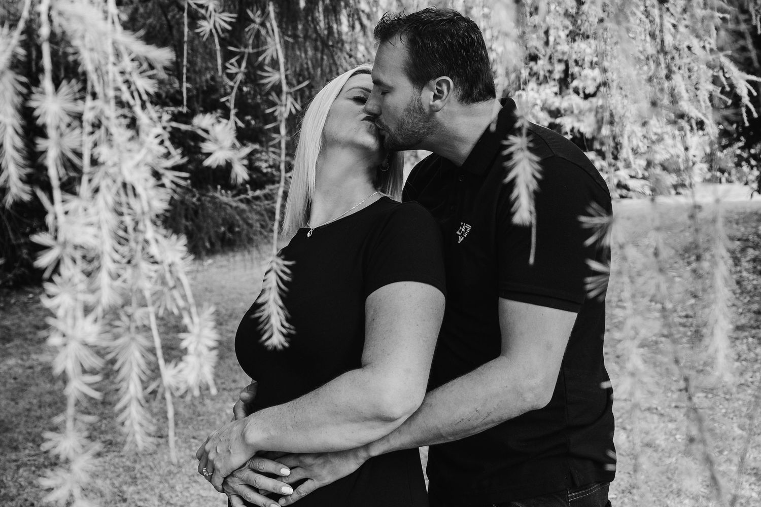 A romantic black and white portrait of a couple embracing outdoors.