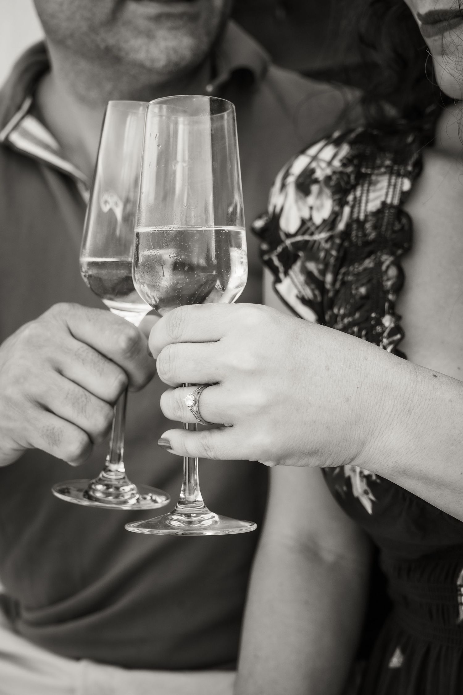 Two wine glasses clinking together in celebration with wedding rings visible.