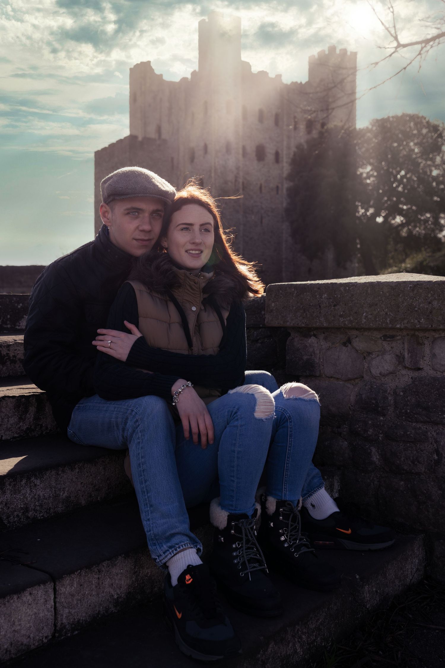 Couple sitting together against historic castle walls at sunset.