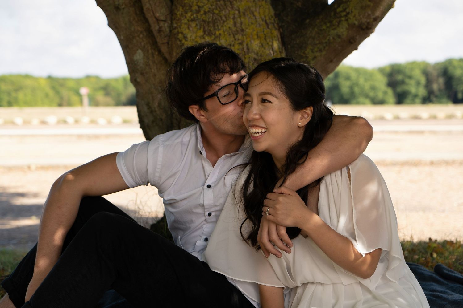 A couple sharing a tender moment while sitting under a large tree.