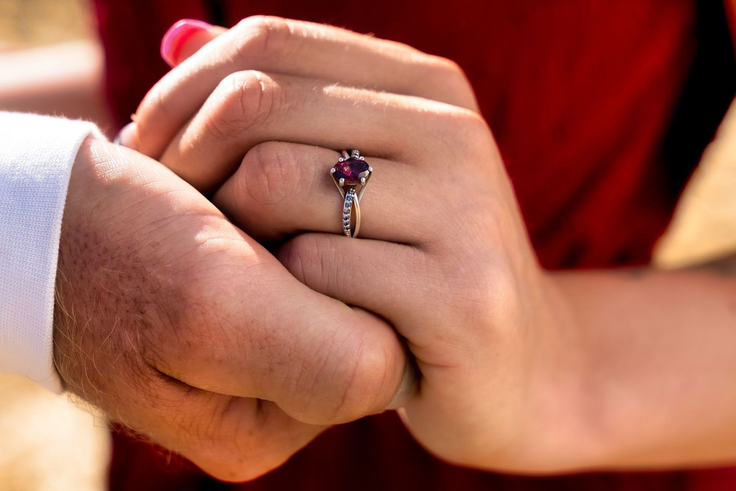 Close-up of hands holding with a purple gemstone engagement ring in focus.