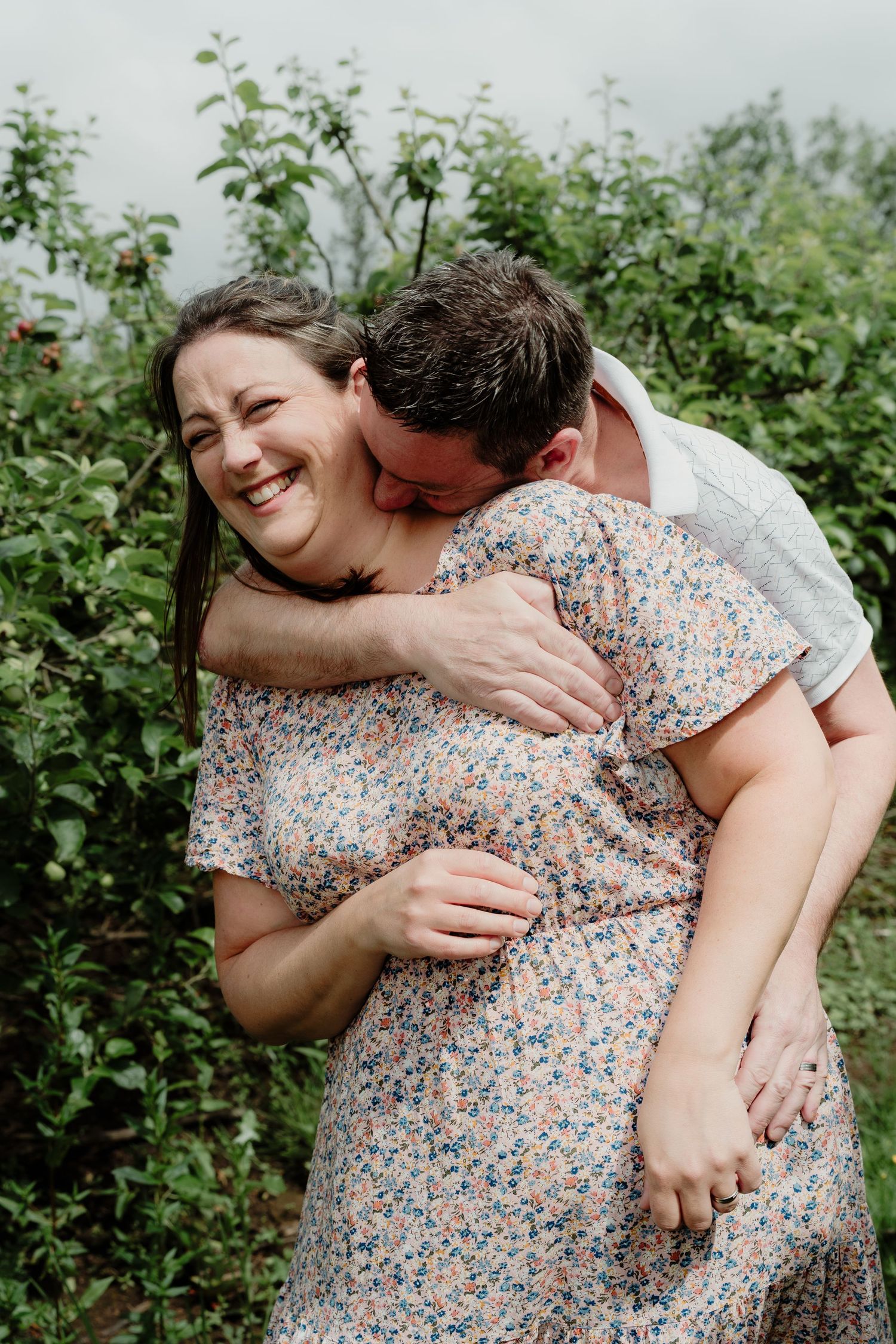 Joyful couple embracing and laughing in a garden with green foliage.
