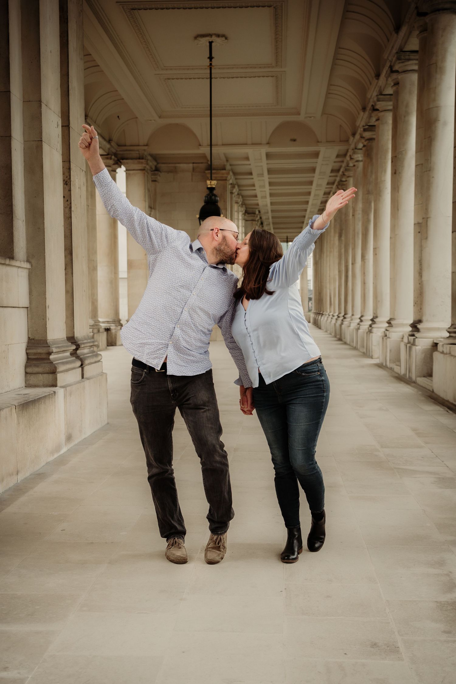 A joyful couple dances and celebrates in a columned hallway wearing matching light blue shirts.