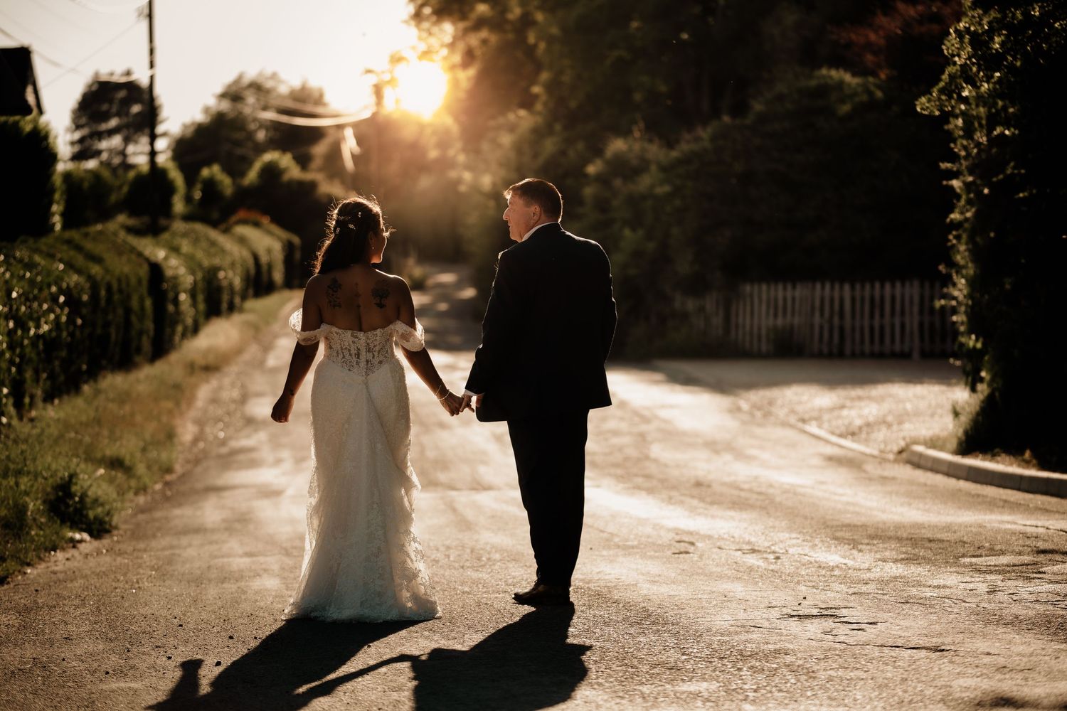 Silhouette of two people holding hands walking down a sunlit dirt road at golden hour.