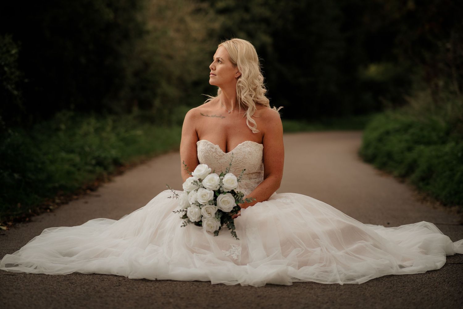 Bride in flowing white wedding gown sitting elegantly in an outdoor garden setting.
