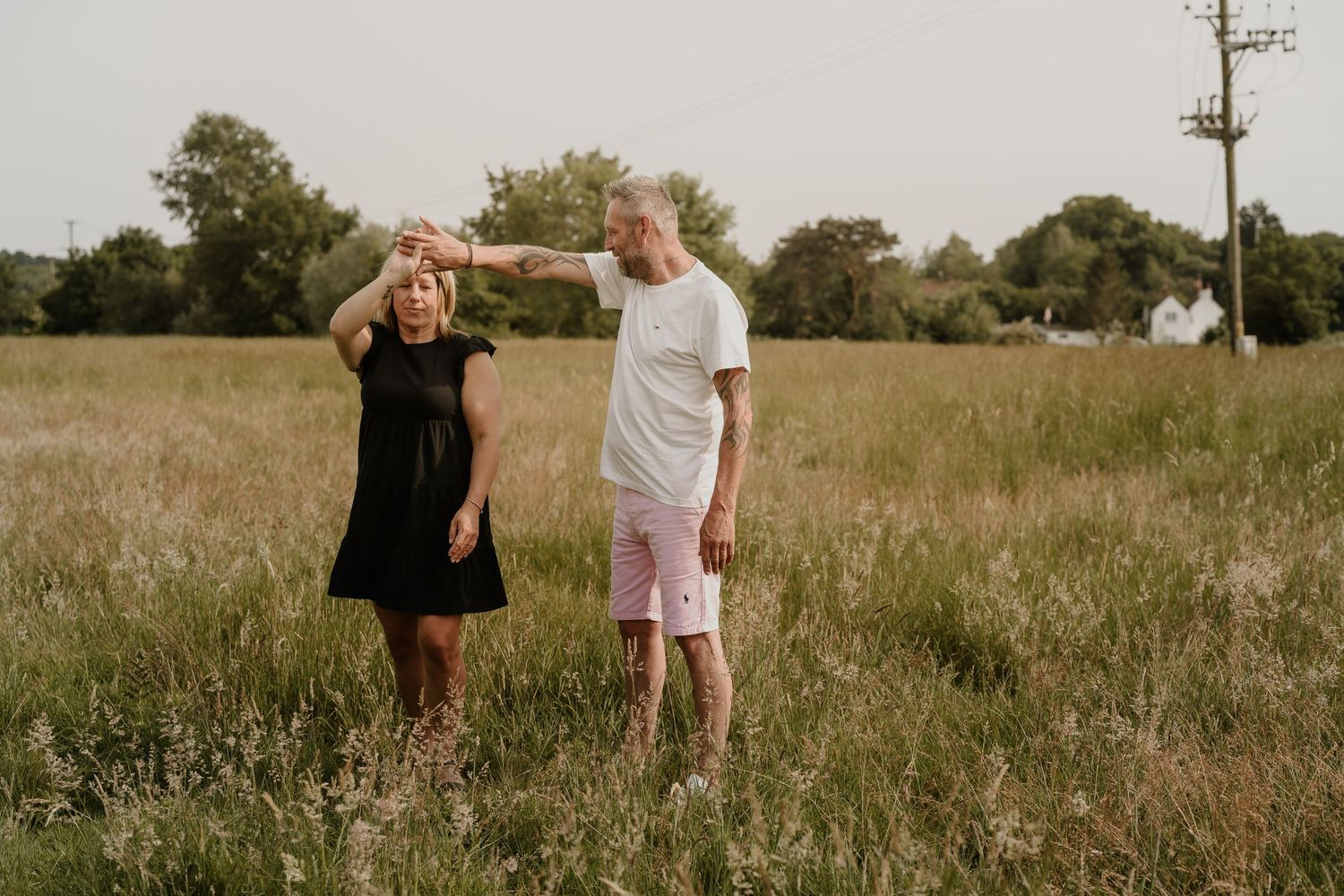 A couple stands together in a golden summer meadow at sunset sharing a candid moment.