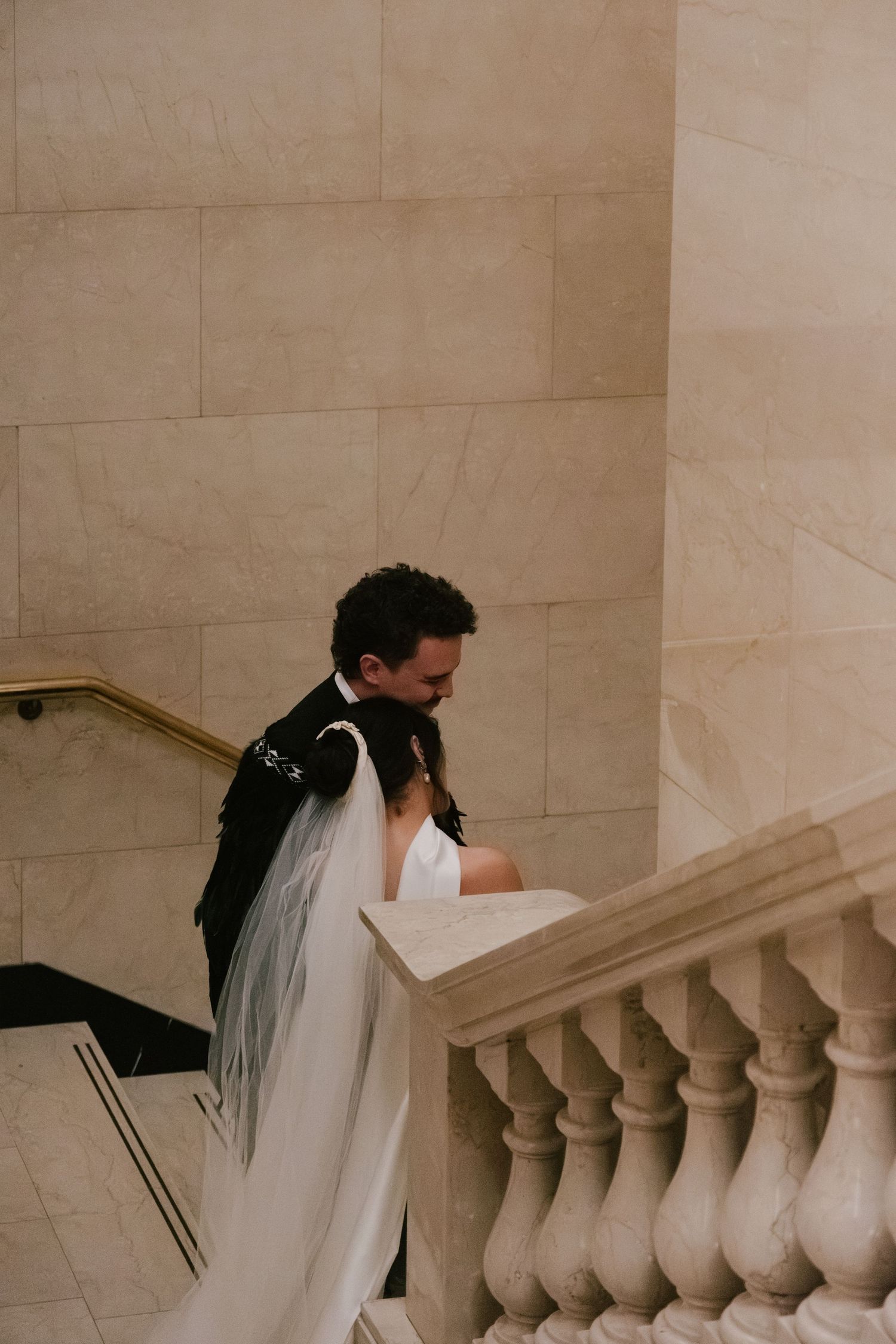 A couple in wedding attire ascends an elegant marble staircase with ornate balustrades.
