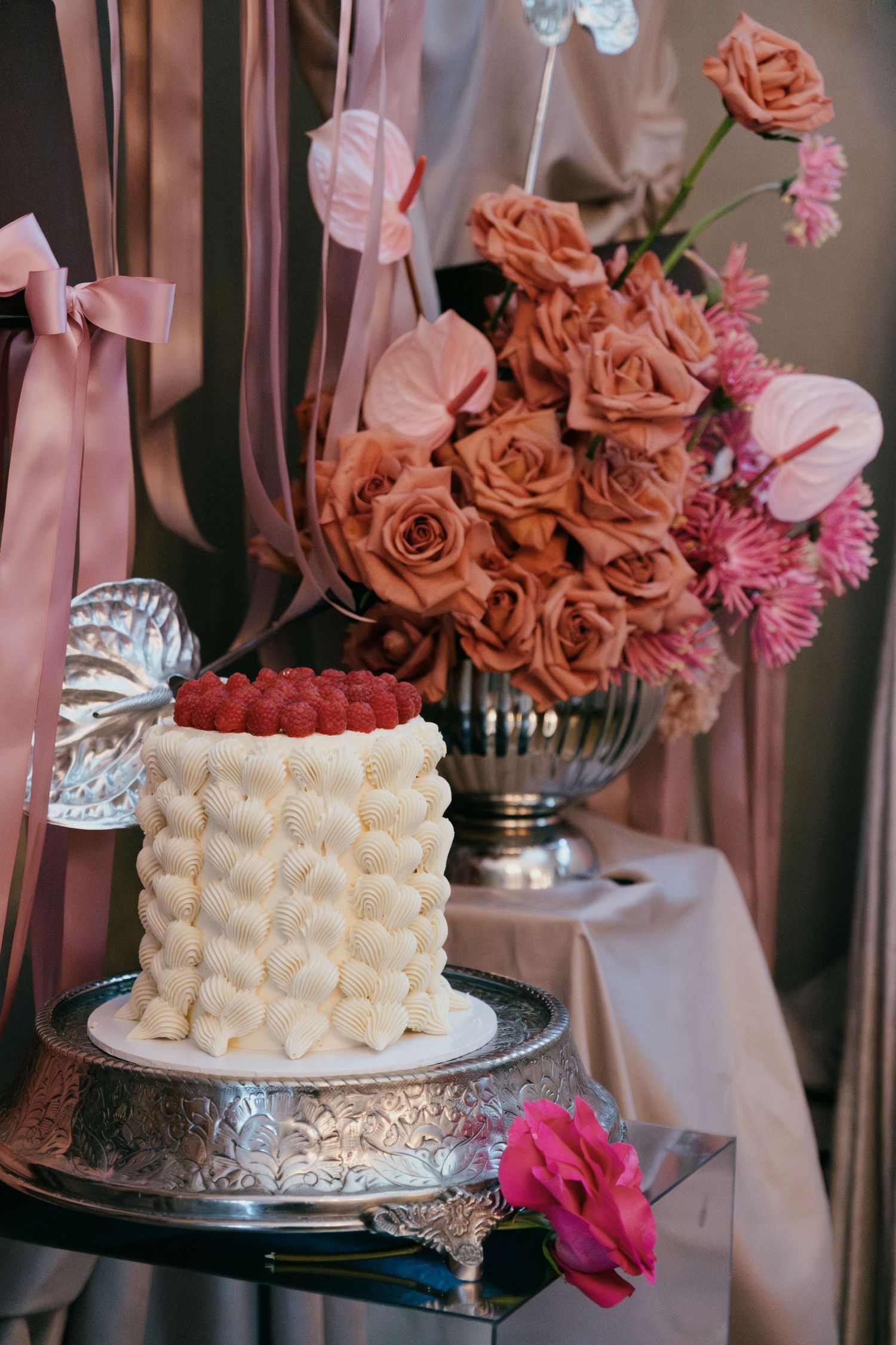 Wedding cake display featuring white buttercream decorations and pink roses with matching floral arrangements.