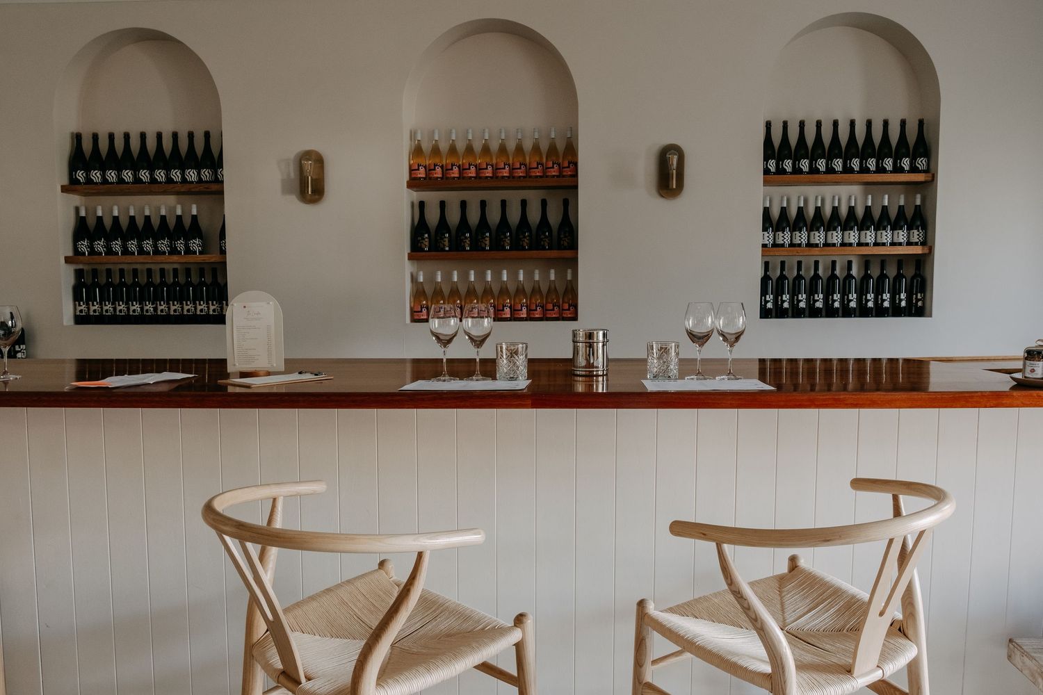 Wine bar interior with bottles displayed on wall shelves and wooden cross-back chairs.