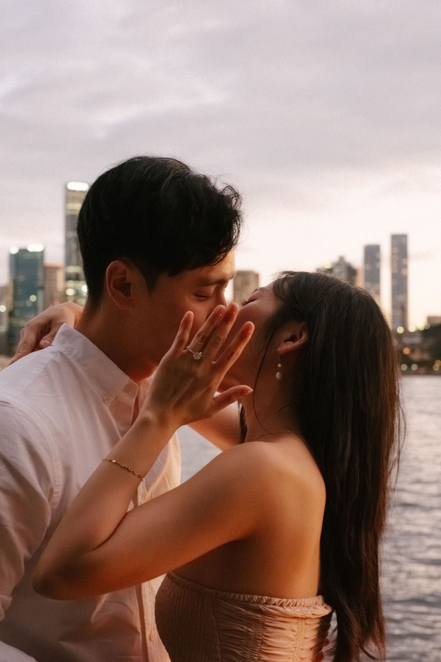A romantic couple shares an intimate moment at sunset with a city skyline in the background.