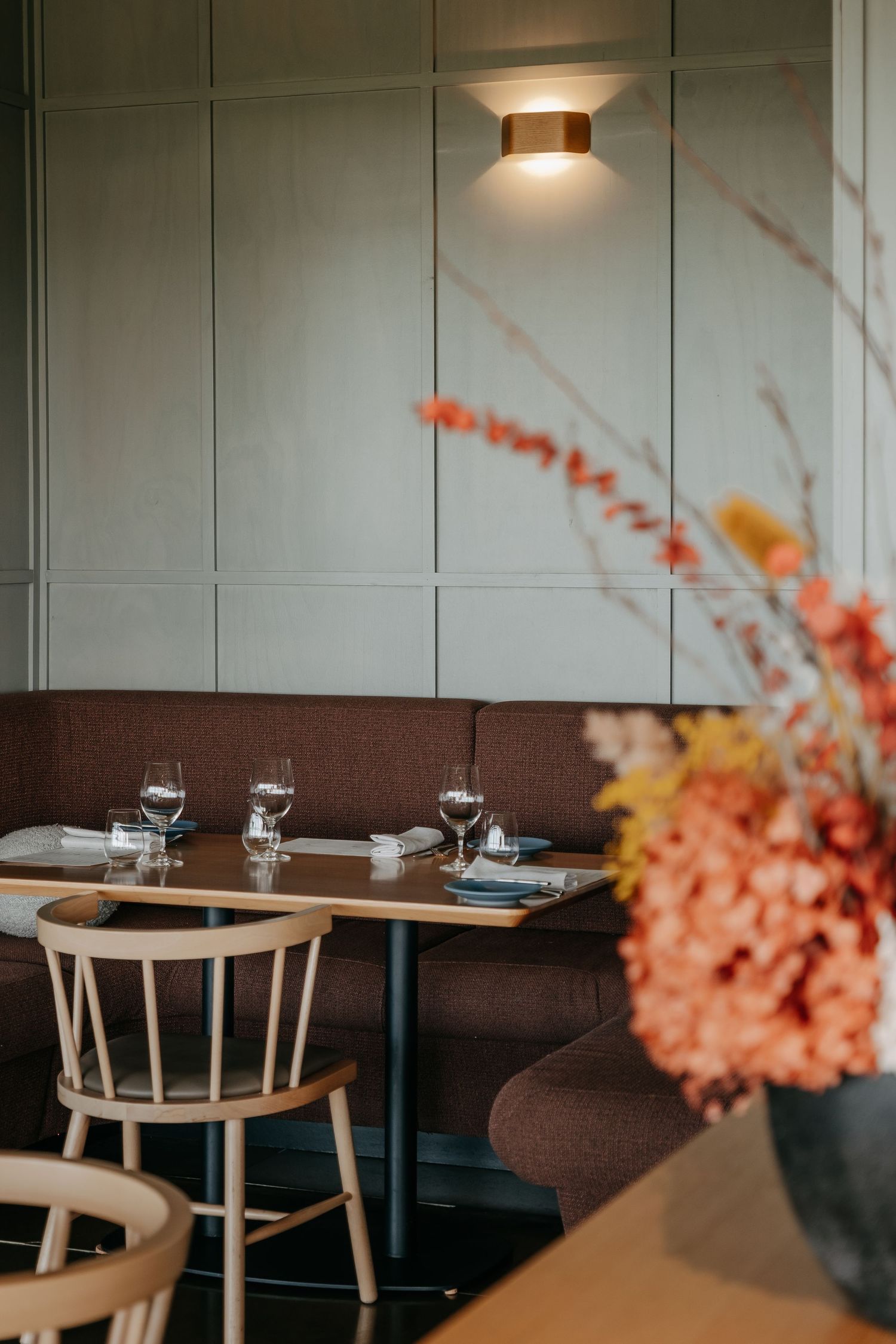 Restaurant dining area with brown booth seating, light wood chairs, and coral flowers in vase.