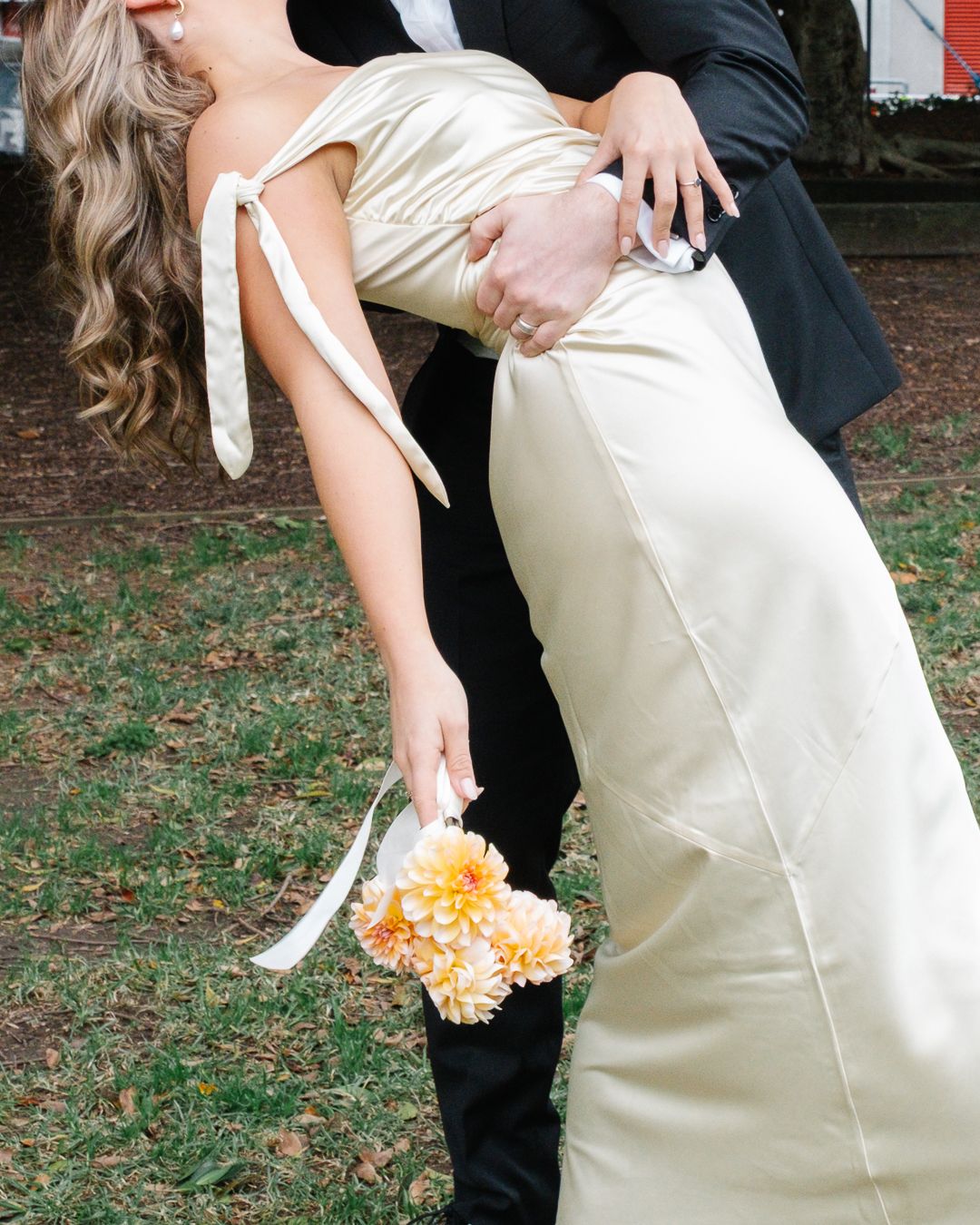 A romantic dip pose at a wedding with the bride in white satin holding orange and peach floral bouquet.