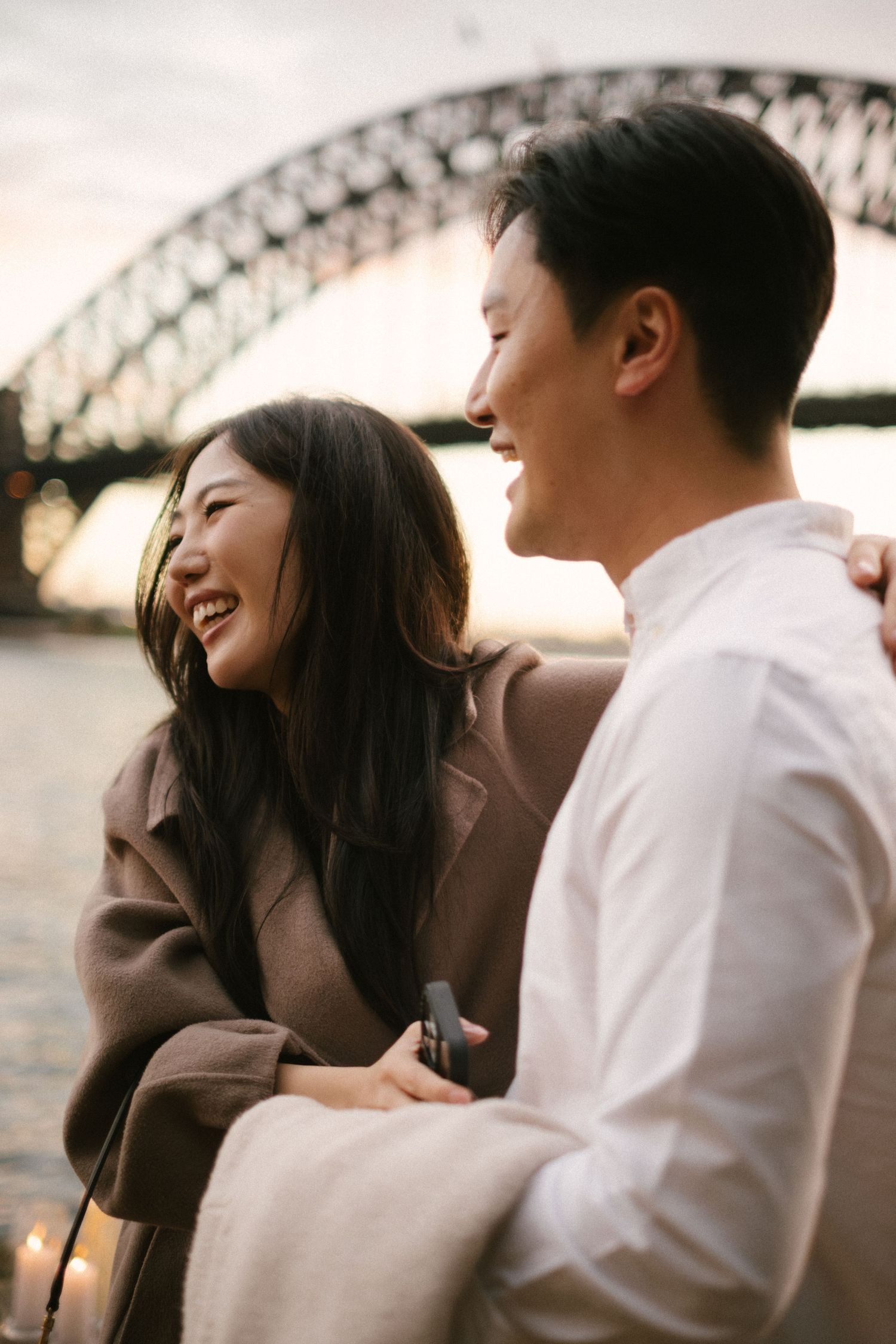 A couple sharing a joyful moment together near Sydney Harbour Bridge during sunset.