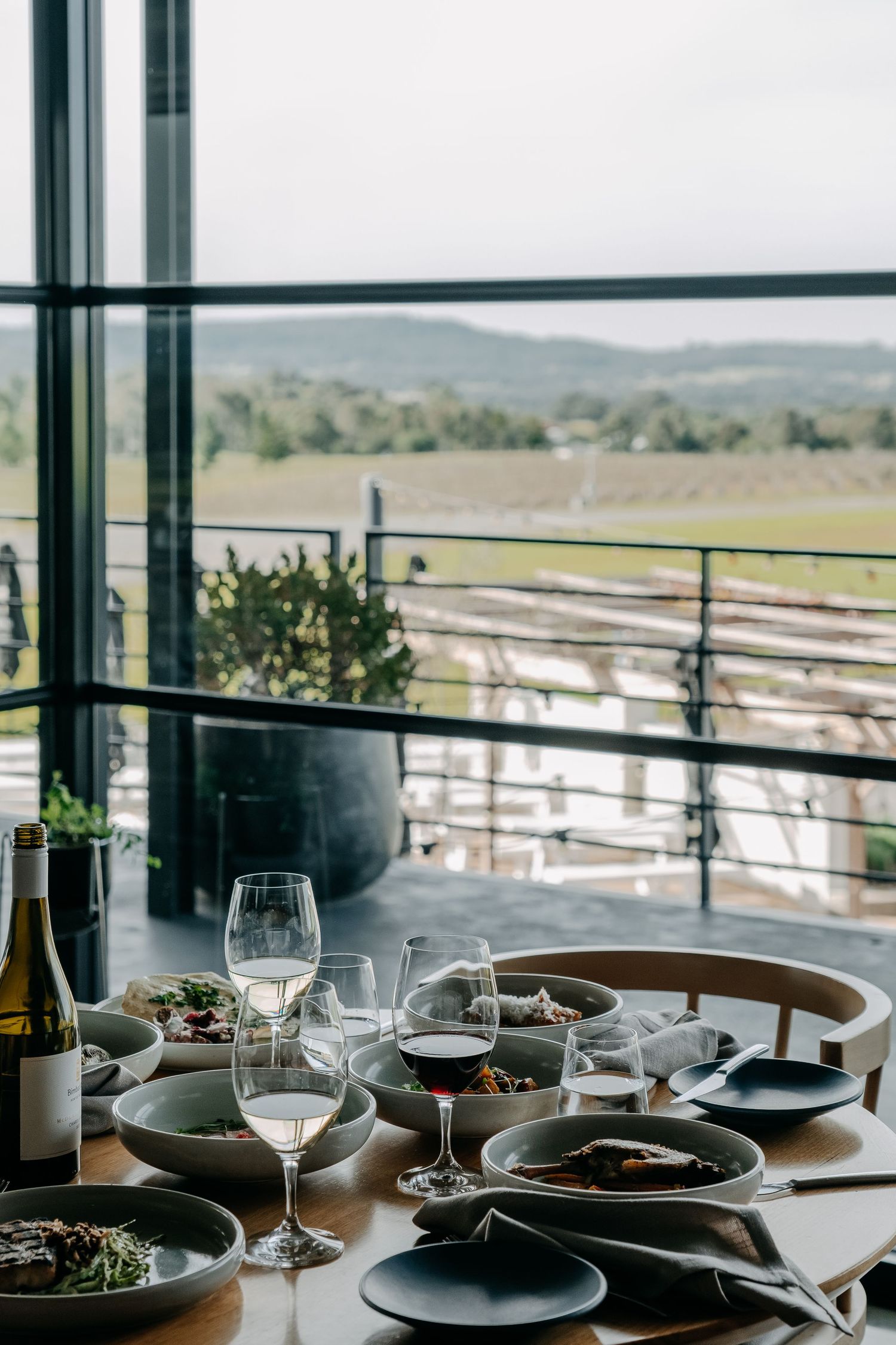 Elegant dining table set with wine glasses and plates overlooking scenic countryside view.