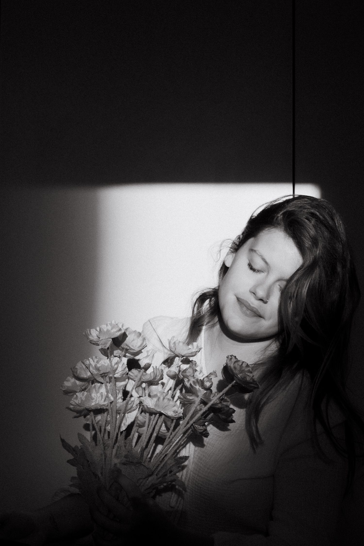 A dramatic black and white portrait shows a person resting near flowers in shadow and light contrast.