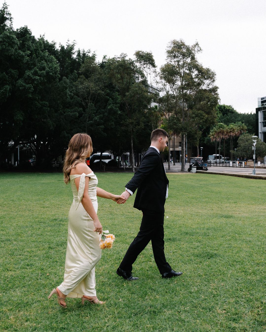 A playful chase sequence unfolds across a grassy field as a couple runs together in formal attire.