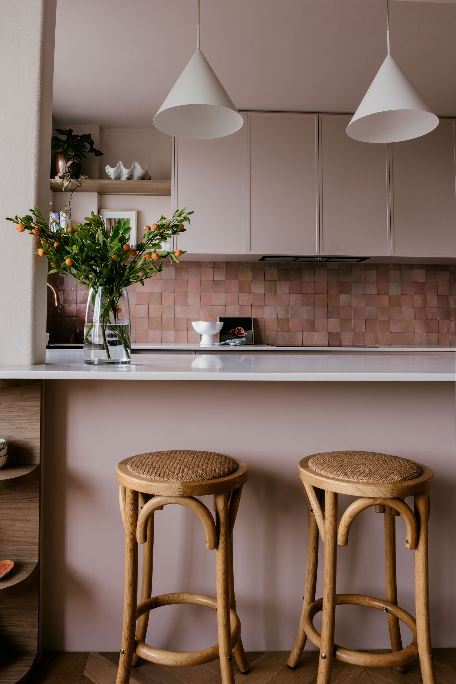 Pink-tiled kitchen with white pendant lights and natural rattan counter stools creating a warm atmosphere.