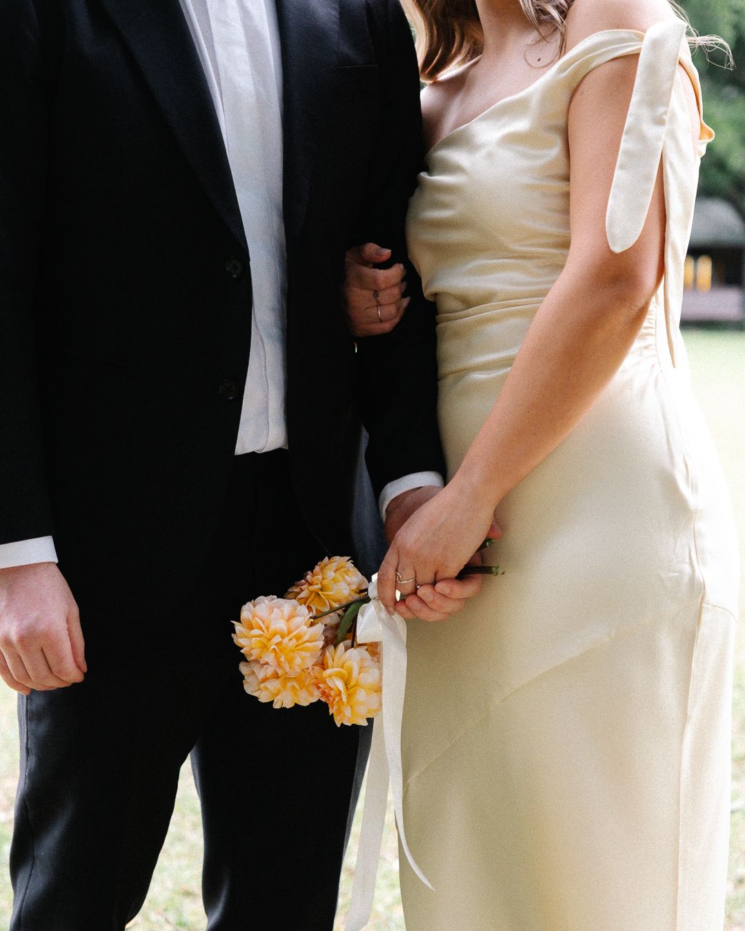 Close-up view of hand and bouquet details showing yellow flowers against elegant wedding attire.