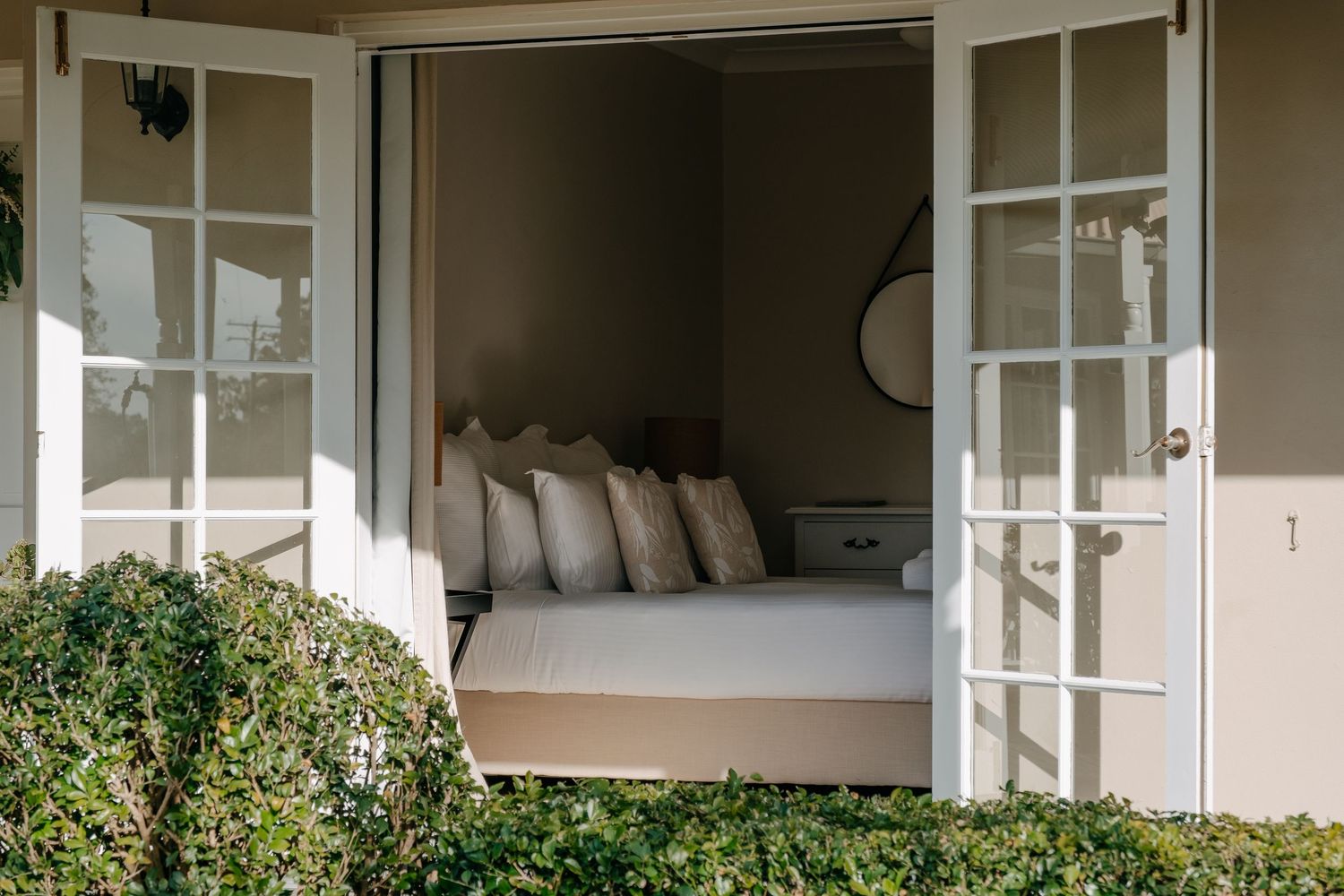 White French doors open to a covered porch with outdoor seating and lush greenery.