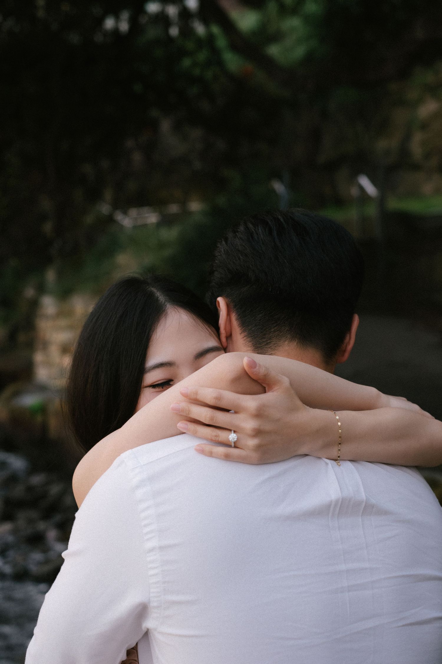 A tender embrace between two people wearing white shirts against a dark natural background.