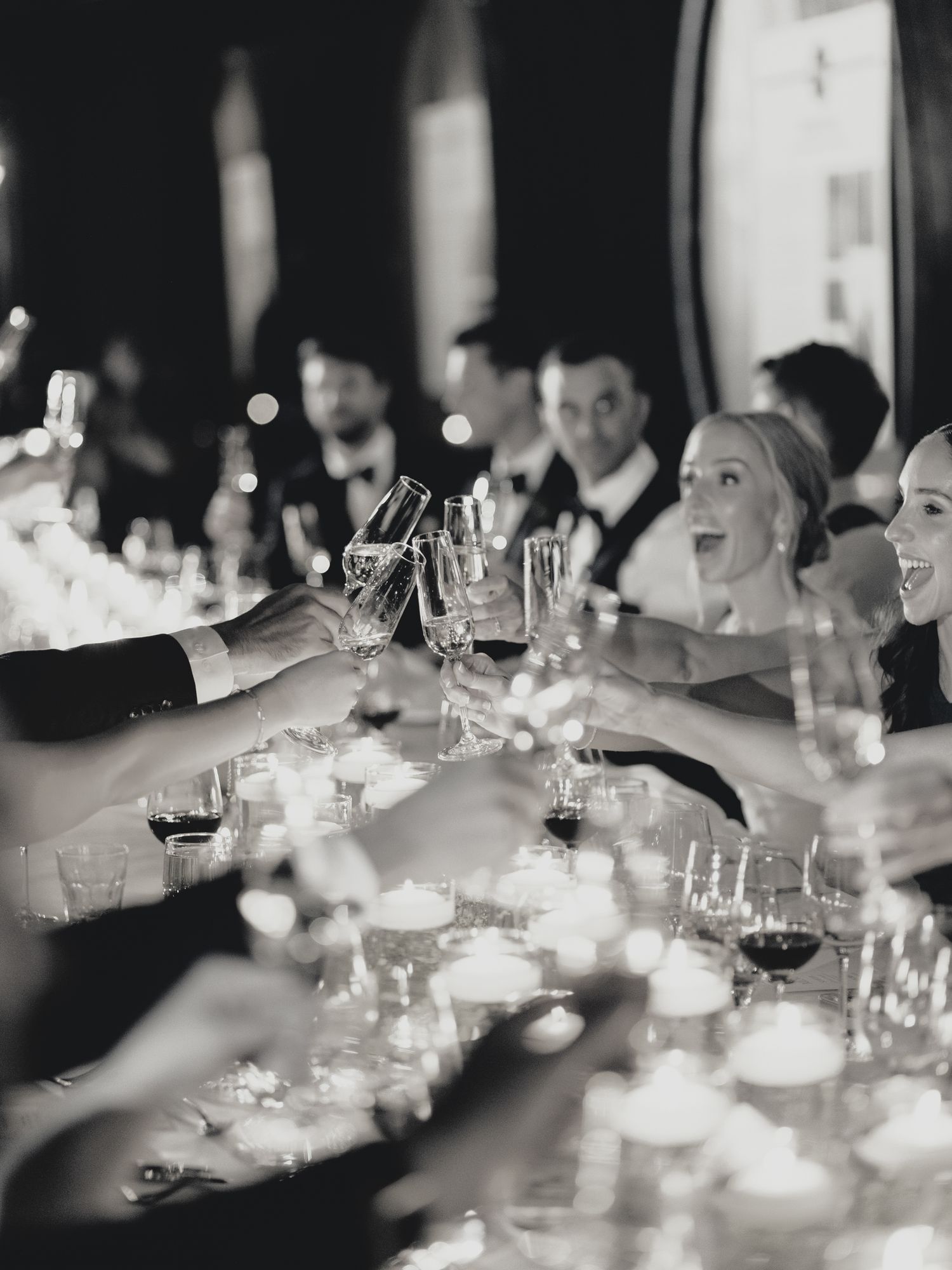 Black and white photo of wedding guests toasting at an elegant candlelit reception table at Greystone in St. Helena.
