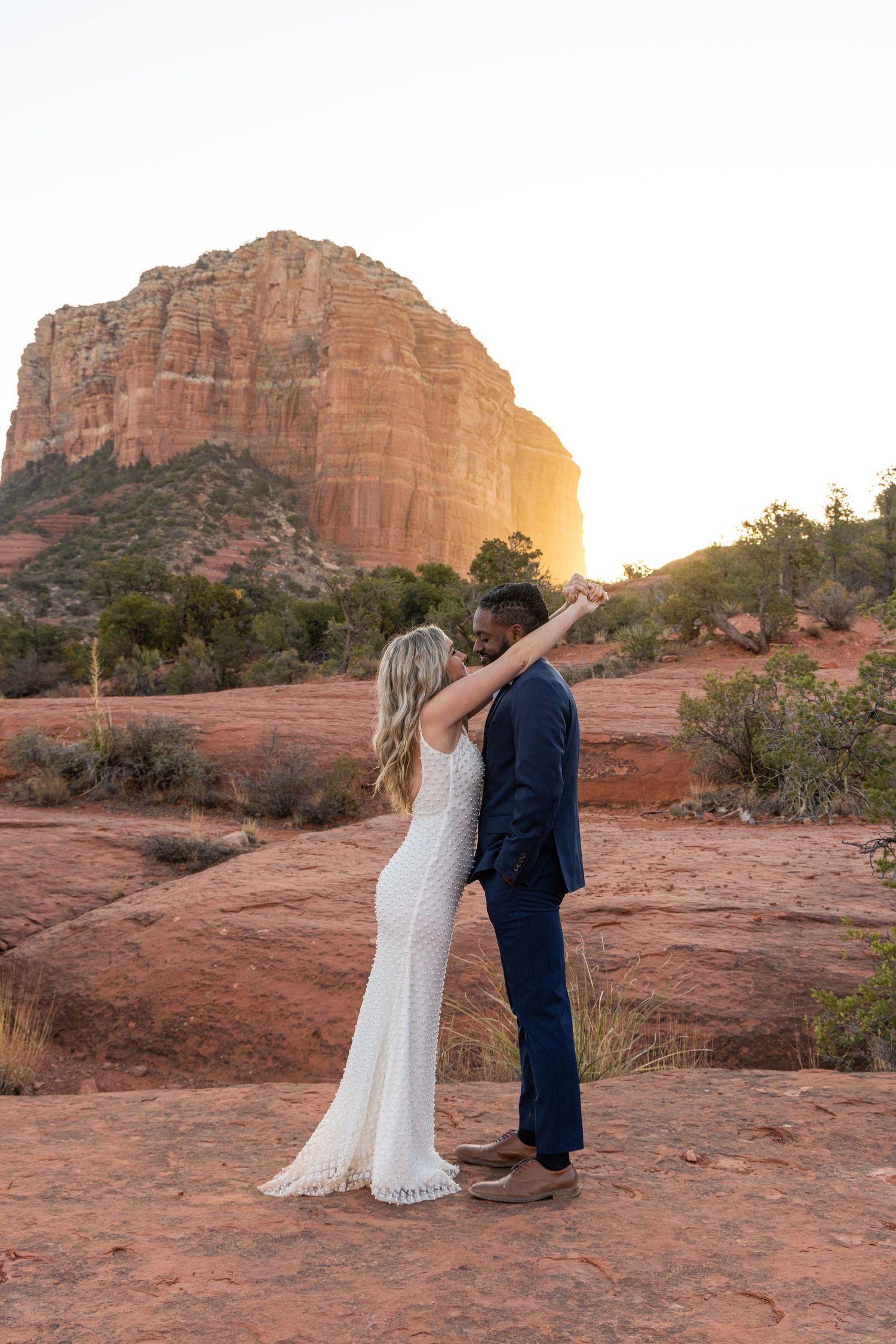 A bride and groom share an intimate moment at sunset in front of a majestic red rock formation in Sedona, Arizona.