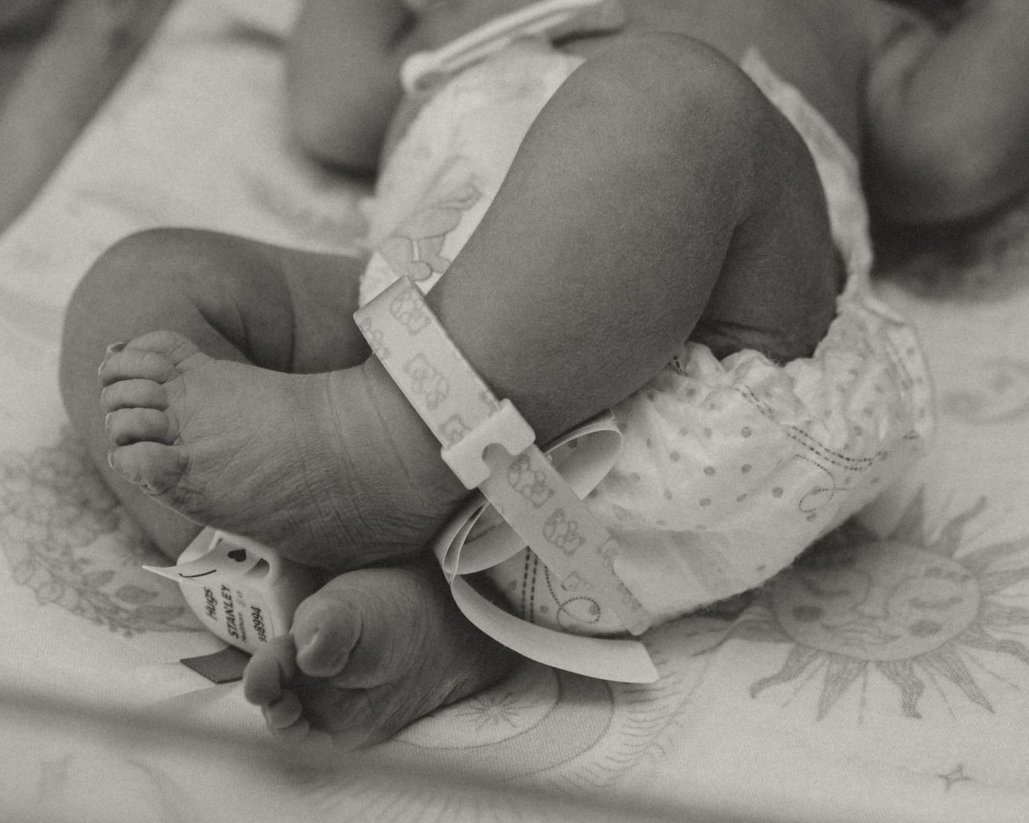 A tiny newborn hand adorned with hospital identification bands rests gently on a crisp white blanket. Fresh 48 Hospital baby Photos in TX