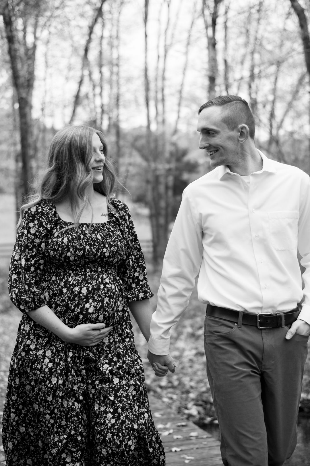Expectant couple shares a joyful moment while walking outdoors in a black and white forest setting.