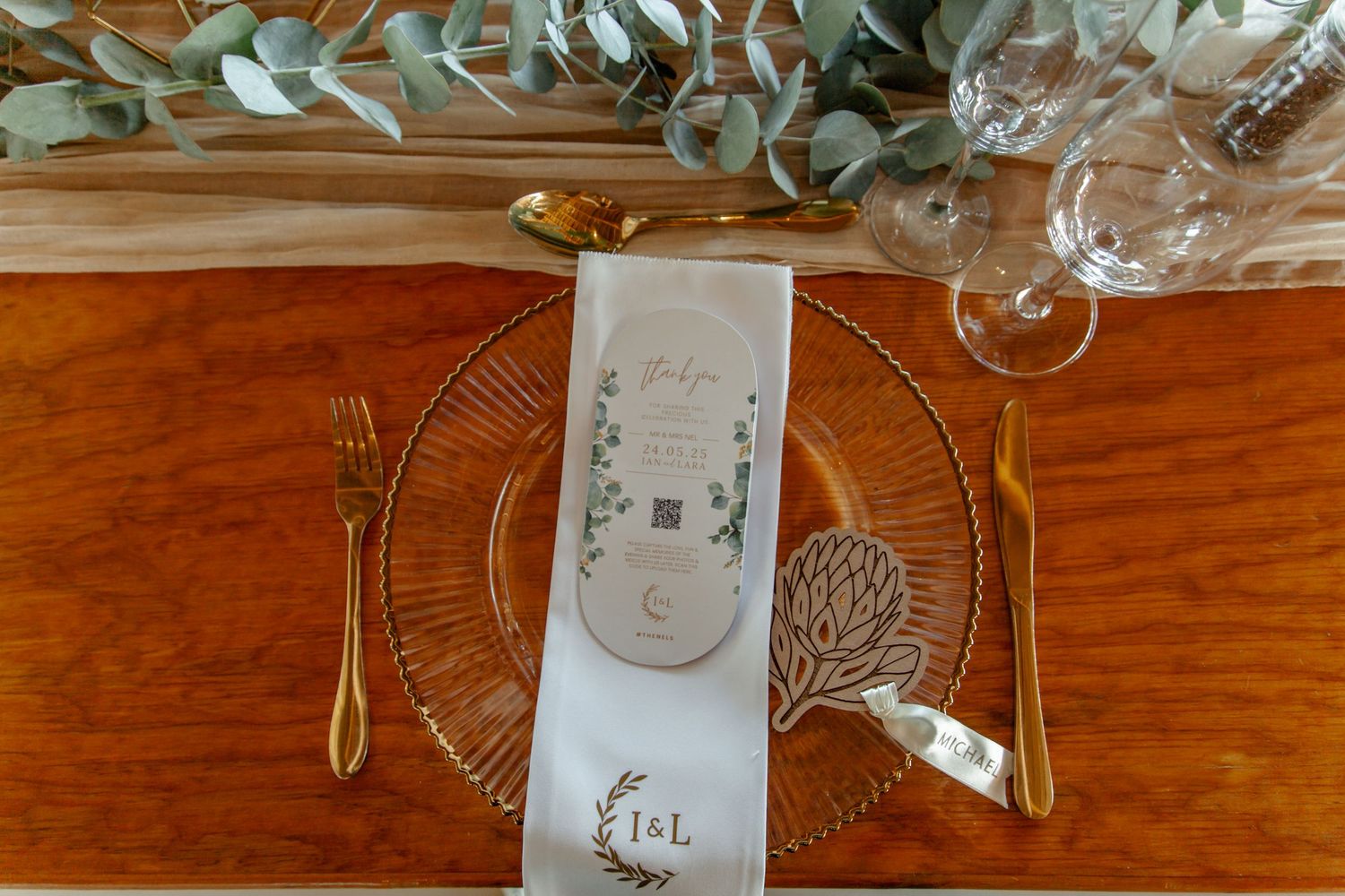 Elegant place setting on wooden table with crystal plate, cutlery, and decorative napkin under greenery garland.