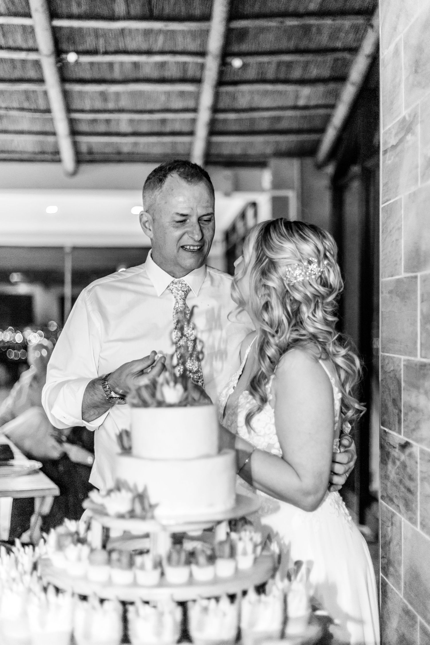 A black and white photo showing a couple cutting their wedding cake together at a rustic reception venue.