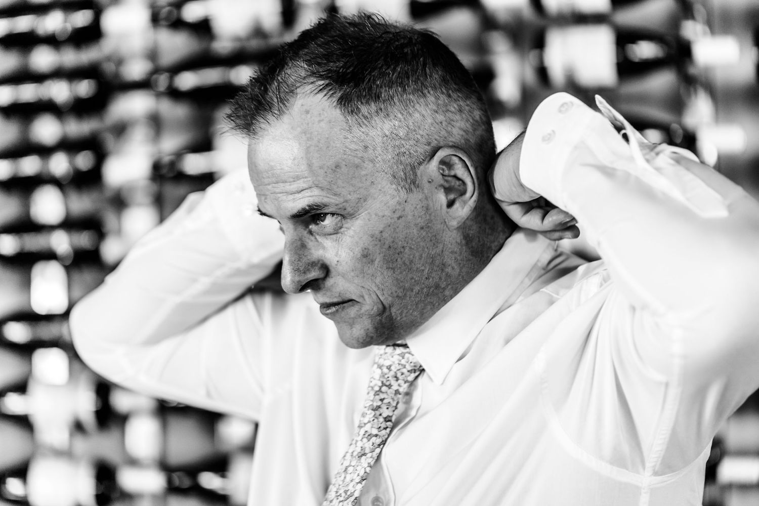 A man in a white dress shirt and polka dot tie looks away while touching the back of his neck.