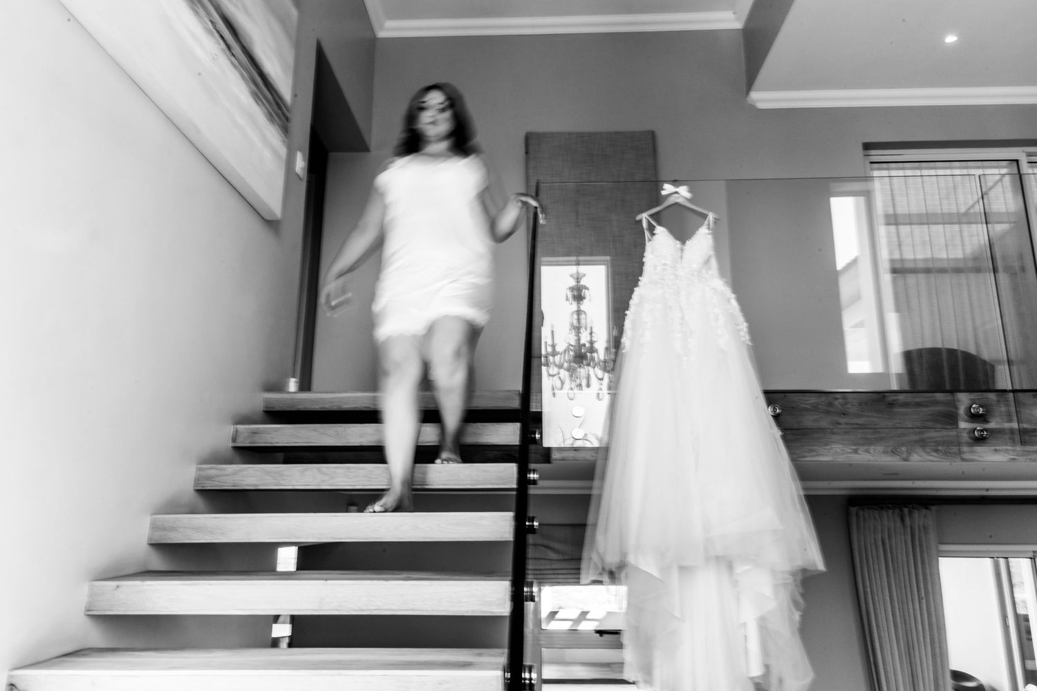 Black and white wedding photograph showing a flowing white wedding gown displayed on stairs and someone descending the steps.