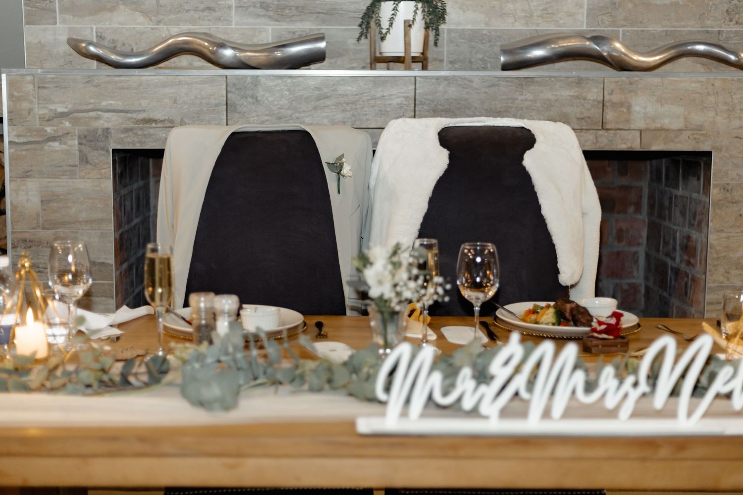 Elegant rustic wedding table setting with black napkins and Mr and Mrs sign against stone fireplace backdrop.
