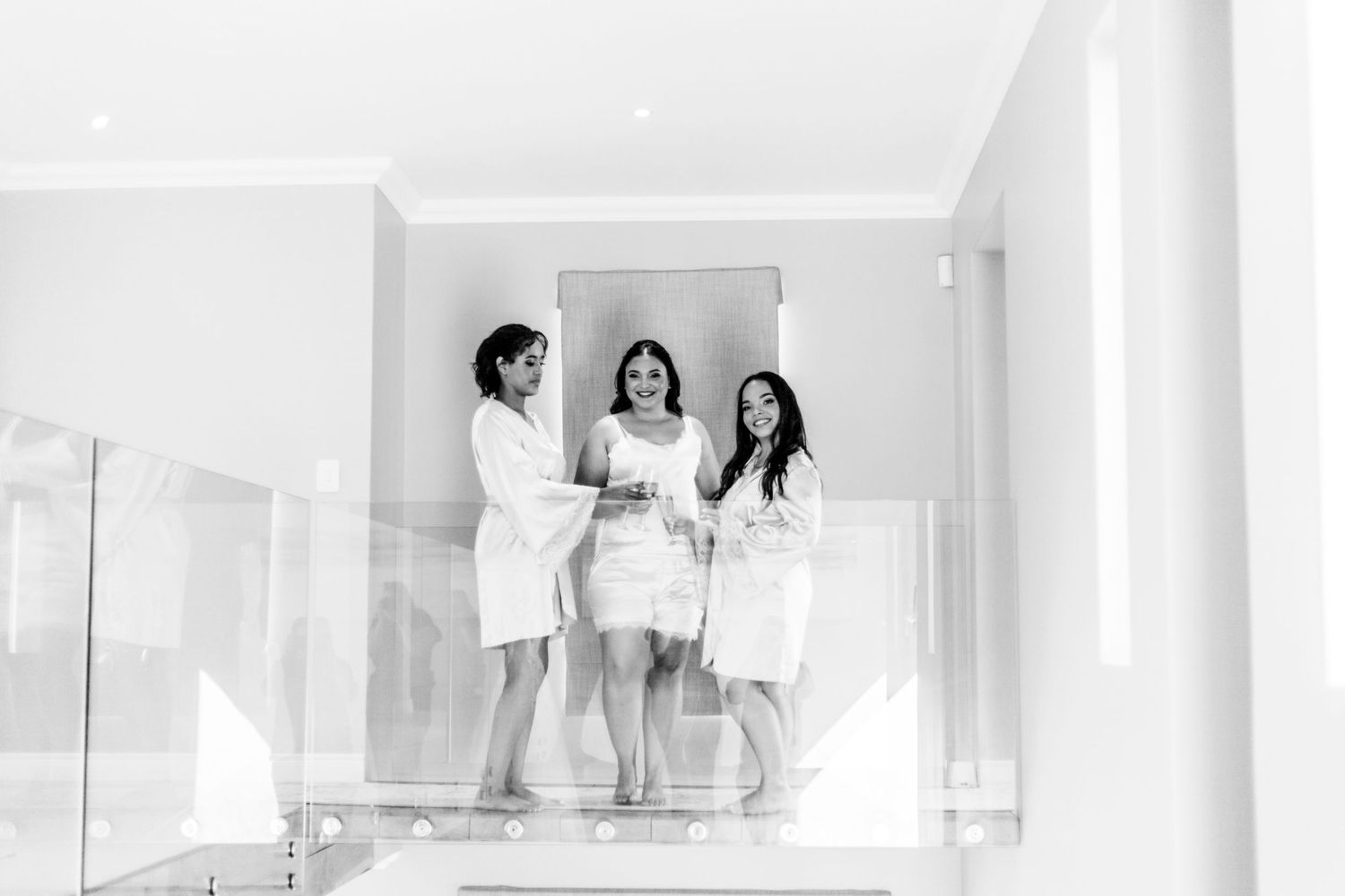 Three people in white robes gather on a bright staircase landing while looking at documents together.
