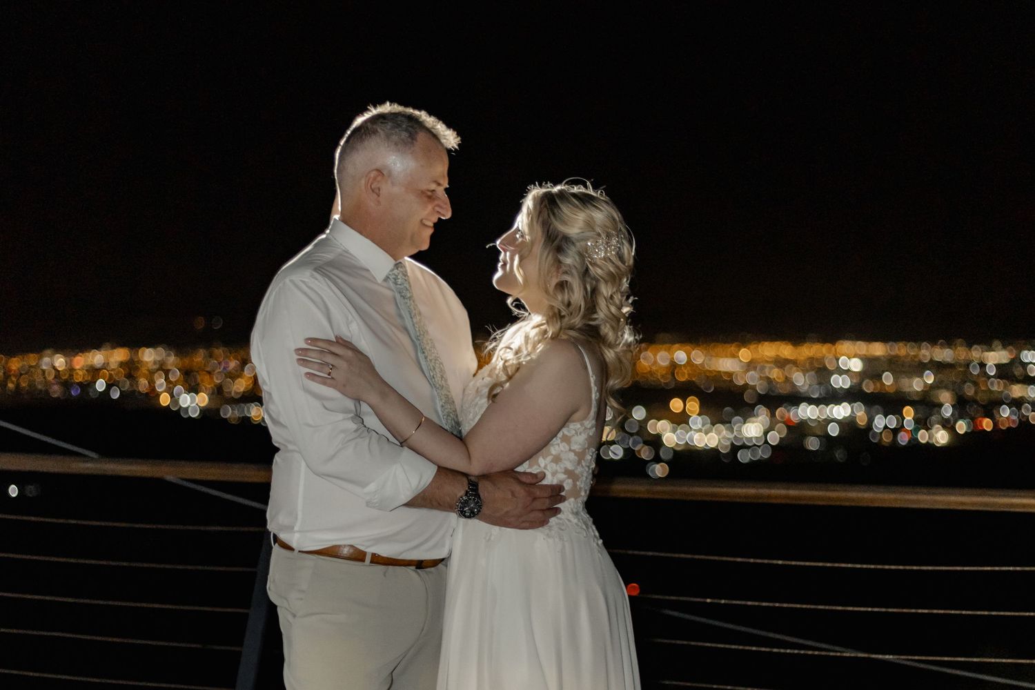A bride and groom dance together at night with city lights twinkling in the background.
