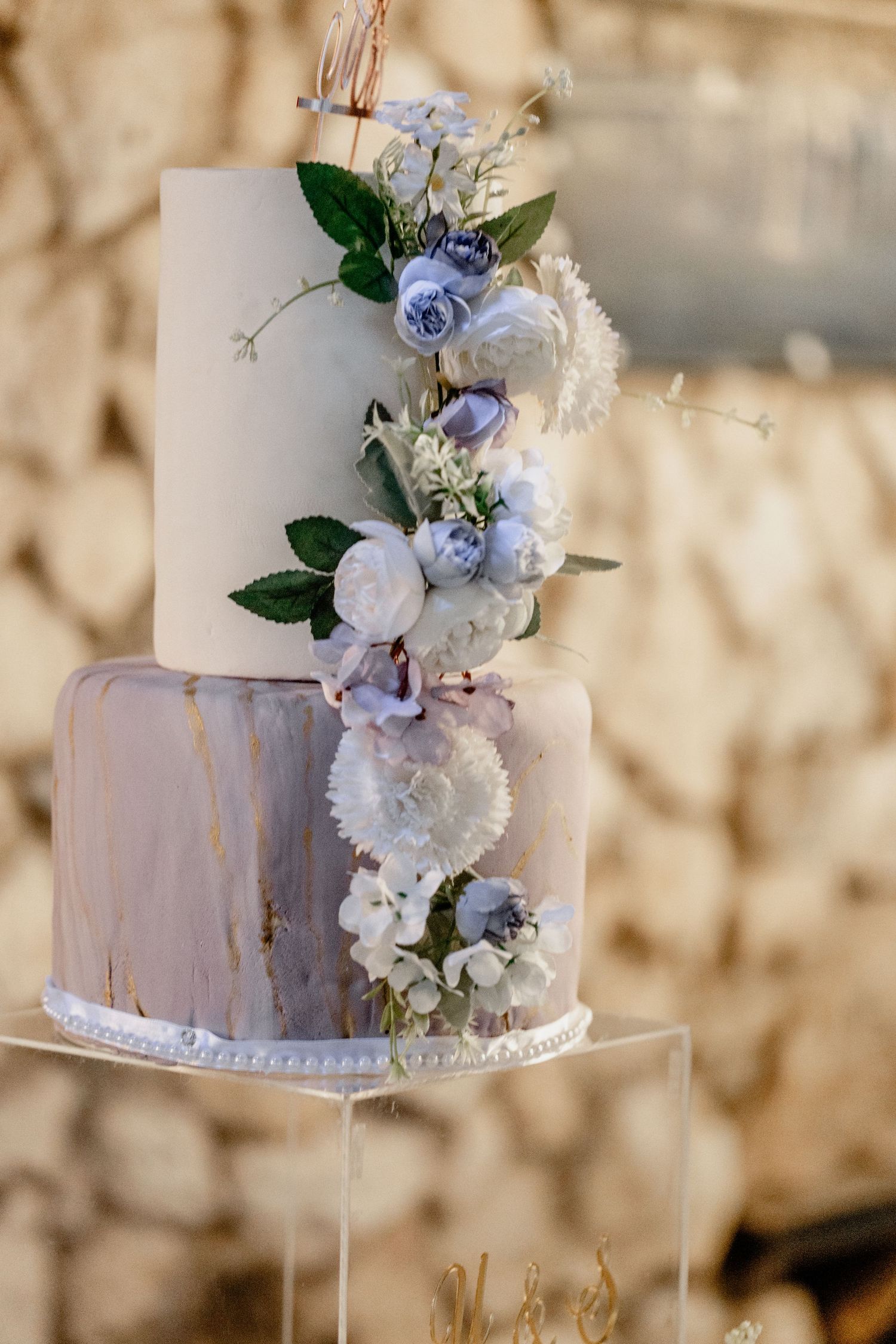 Elegant two-tier wedding cake decorated with blue and white flowers, marble effect fondant, and floral cascade arrangement.
