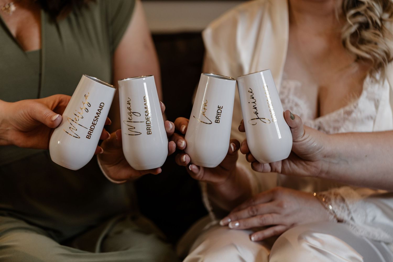 Four hands hold customized white tumblers while toasting during a wedding celebration.