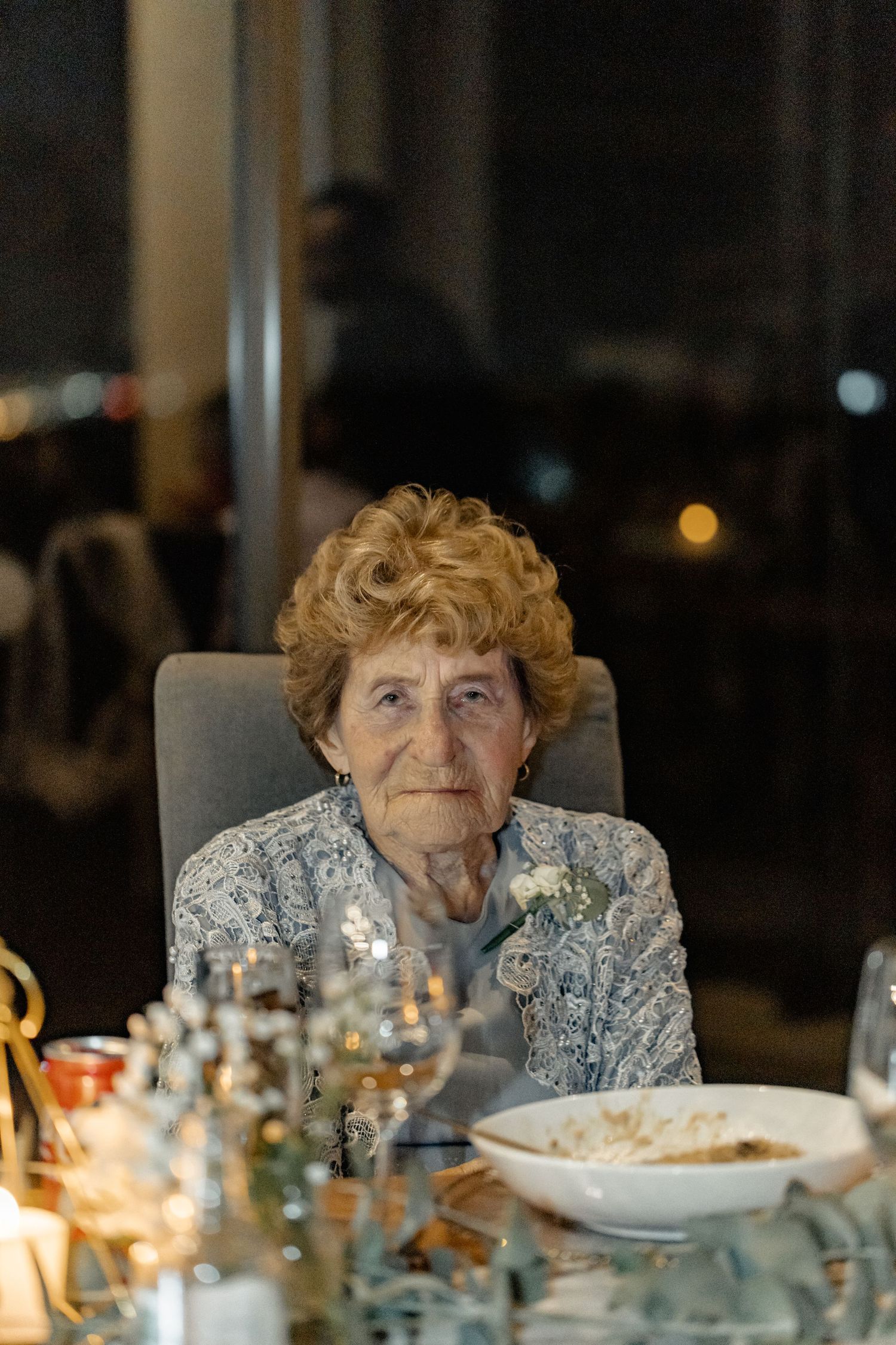 Person seated at elegant dinner table with candles and place settings in evening lighting.
