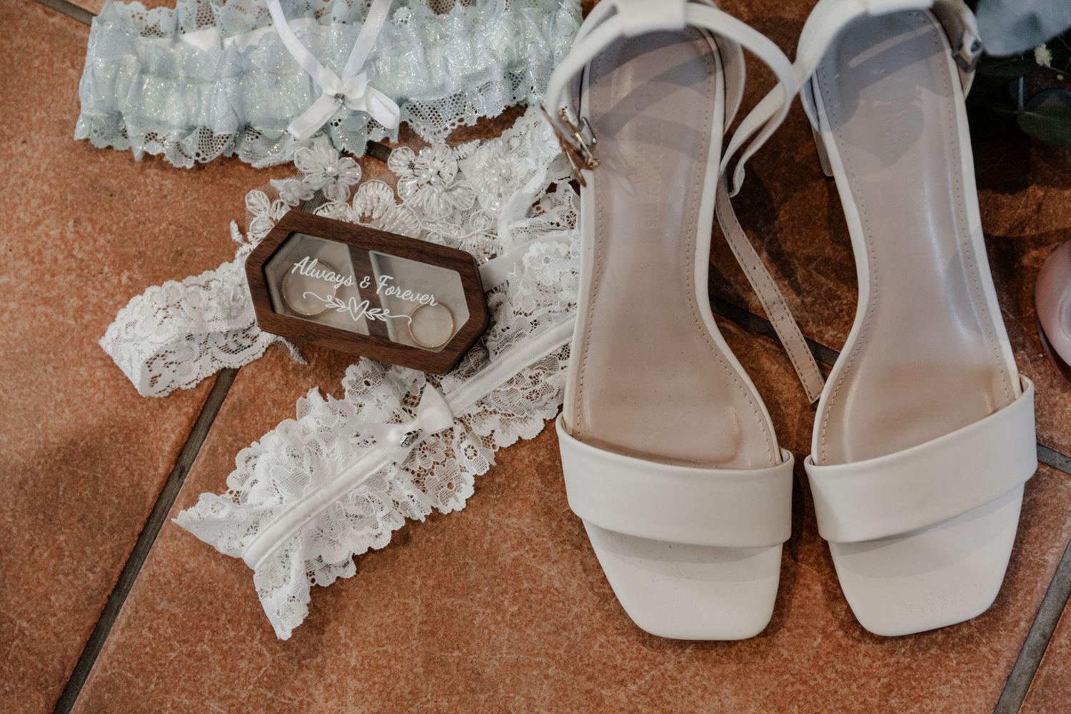 White wedding shoes and lace garter with antique key displayed on terracotta surface for bridal details photography.