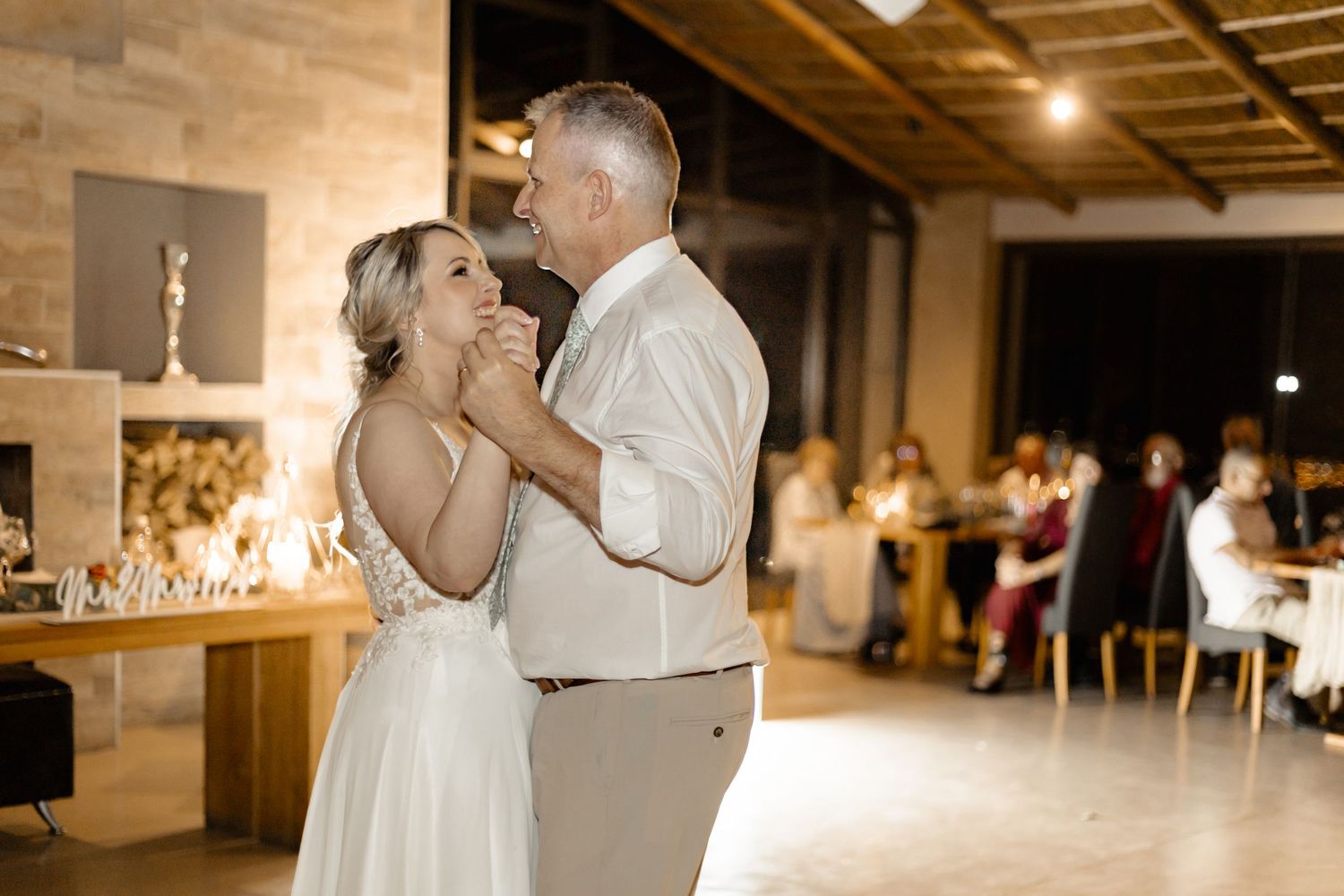 A couple share an intimate first dance in a rustic reception venue with candlelit tables in the background.