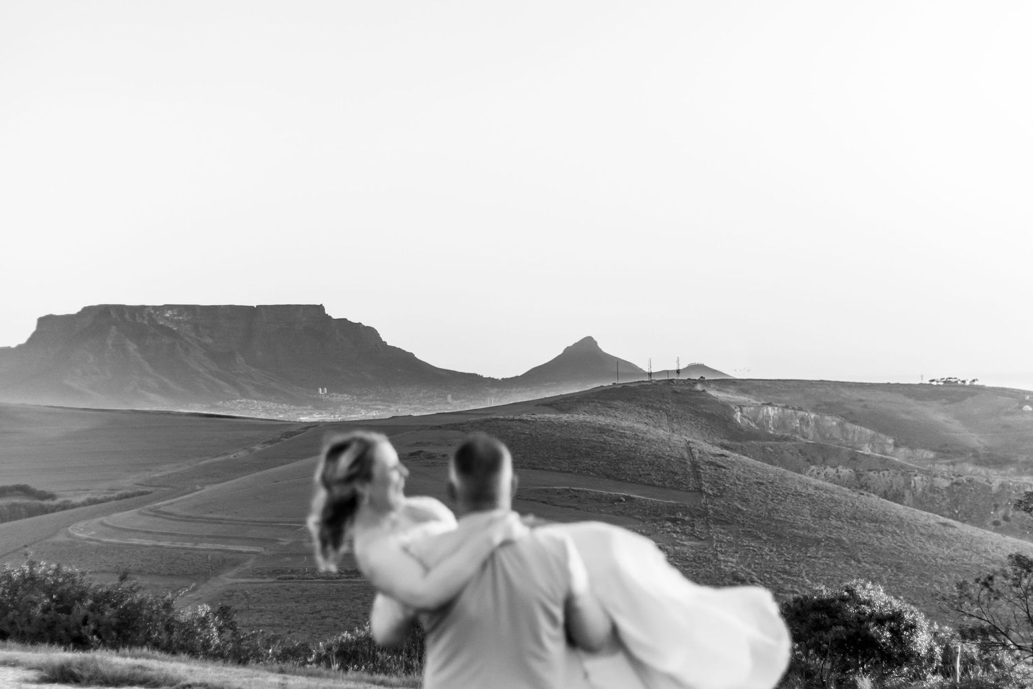 A monochromatic landscape photo featuring silhouettes overlooking a mountainous vista with dramatic peaks and valleys.