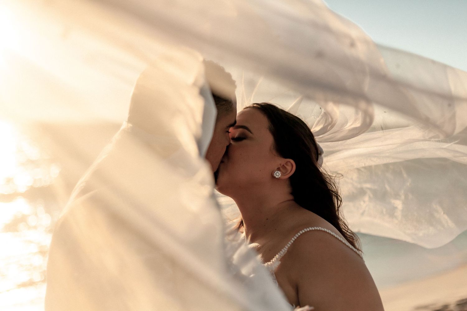 A flowing white veil billows in the breeze during a golden sunset photoshoot.