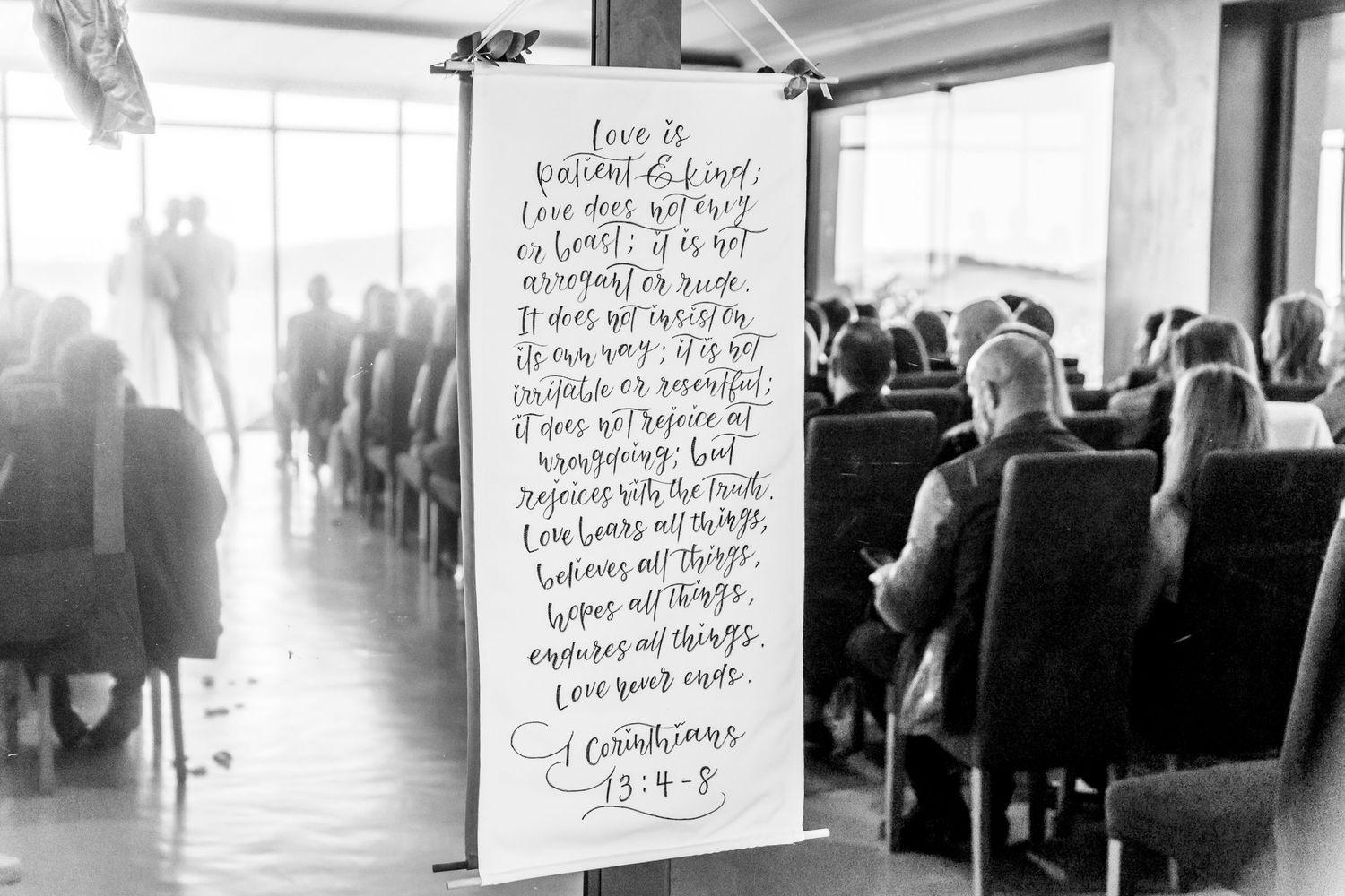 A handwritten note hangs from a window in a crowded restaurant, with blurred diners visible in black and white.