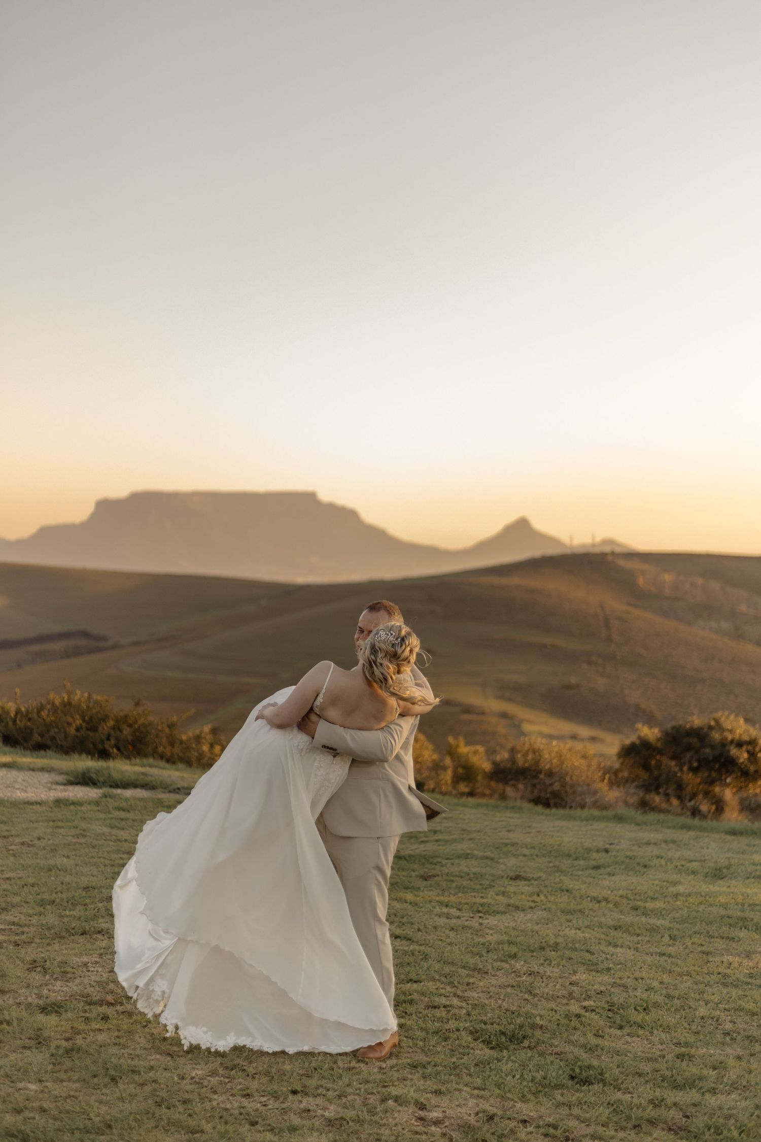 Wedding dress flowing in the breeze against a mountainous landscape at golden hour sunset.
