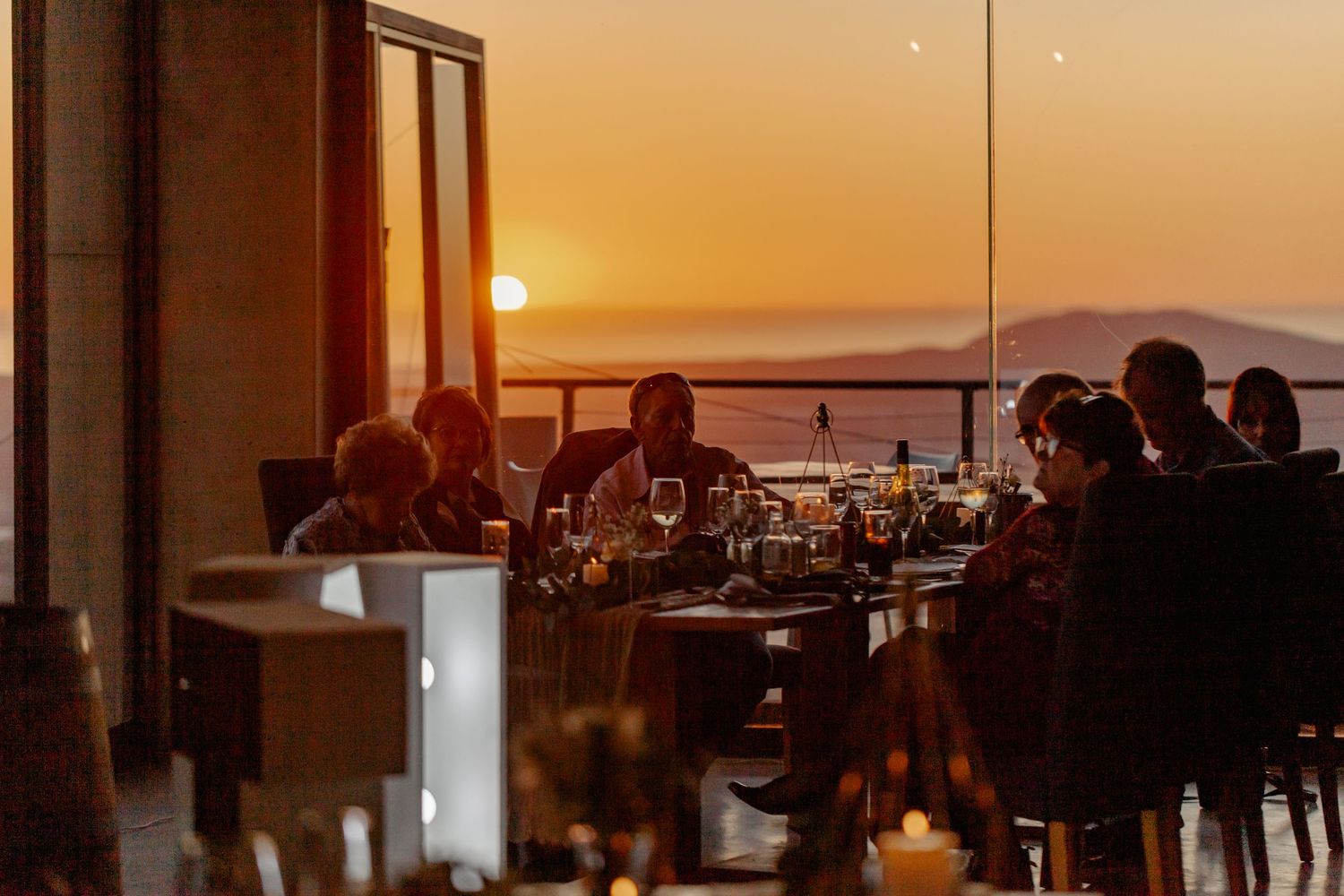 Diners enjoy a sunset meal at an upscale restaurant with panoramic mountain views through floor-to-ceiling windows.